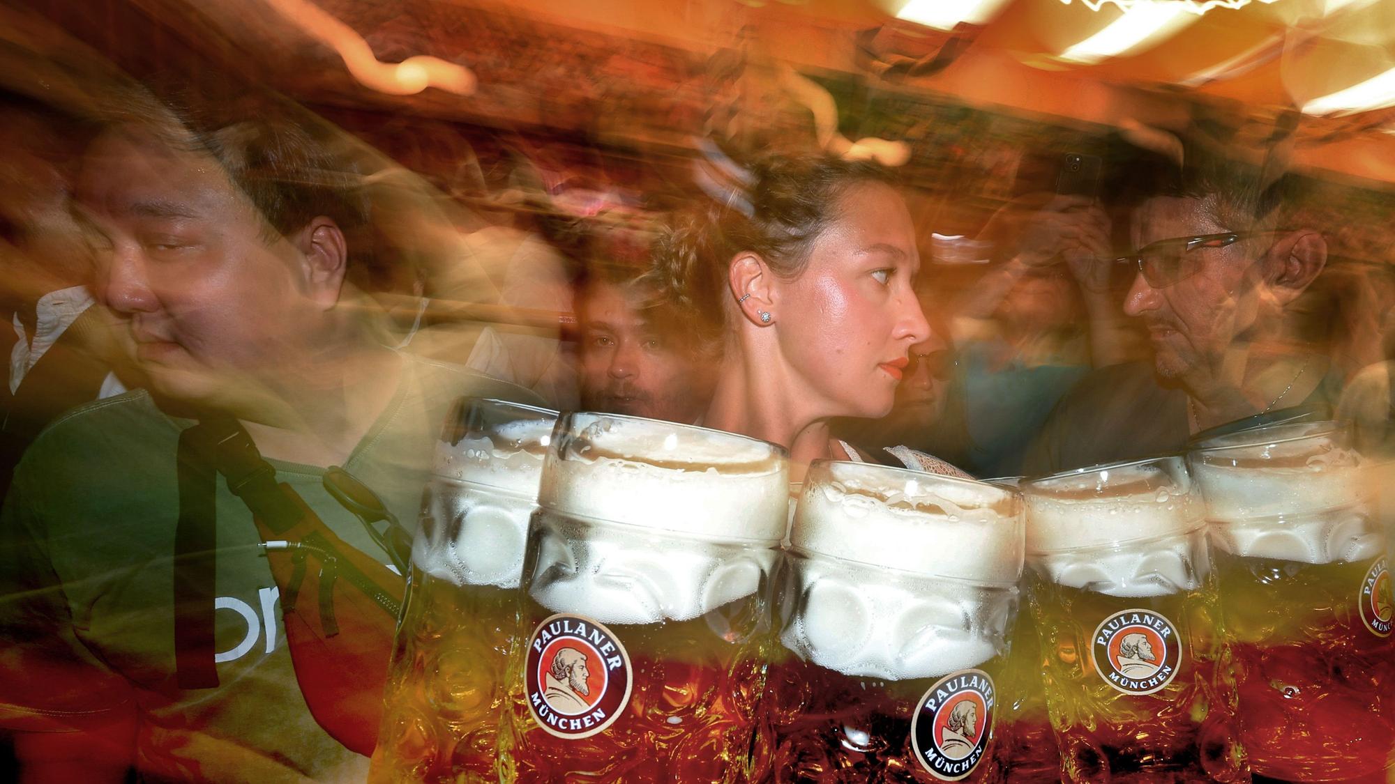 Eine Bedienung trägt im Paulaner-Festzelt Maßkrüge mit Bier (Unschärfe durch lange Belichtungszeit).