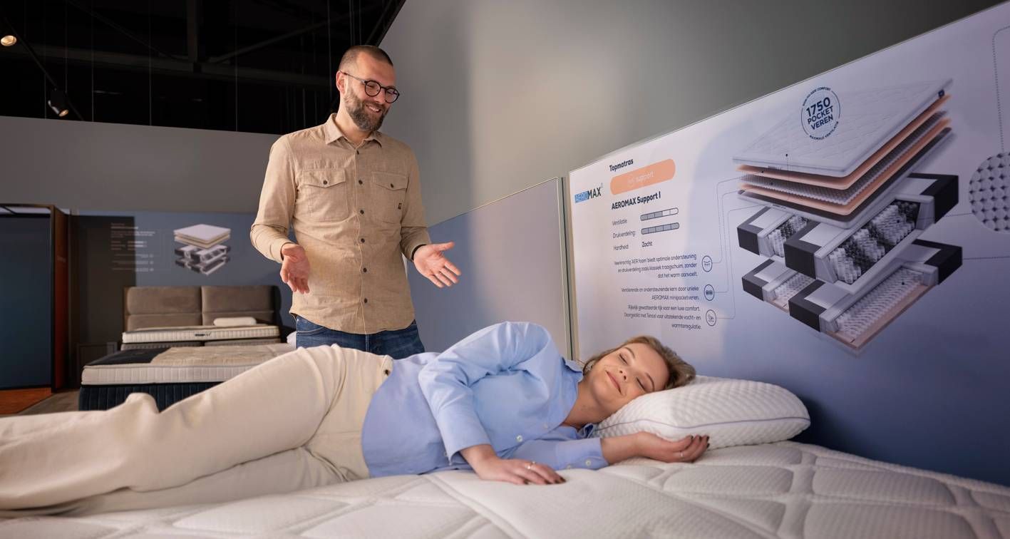 Eine Frau testet im Showroom auf einer Matratze den Liegekomfort, während ein Schlafberater berät.