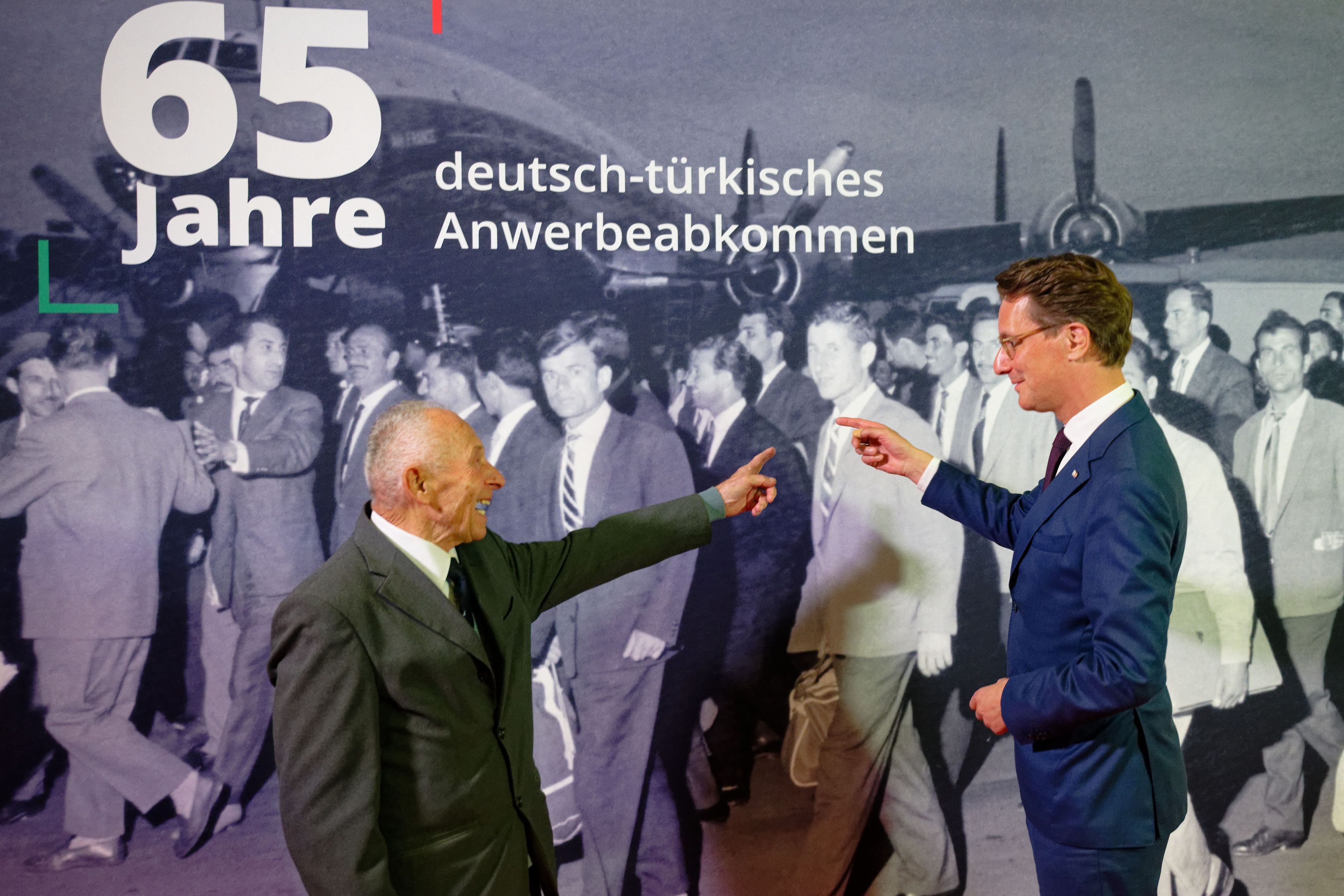 Hendrik Wüst (CDU), Ministerpräsident von Nordrhein-Westfalen, spricht bei einer Festveranstaltung zum 65. Jubiläum des Anwerbeabkommens mit der Türkei am Düsseldorfer Flughafen mit Sabri Aydin (l) der vor 65 Jahren hier aus der Türkei angekommen ist.