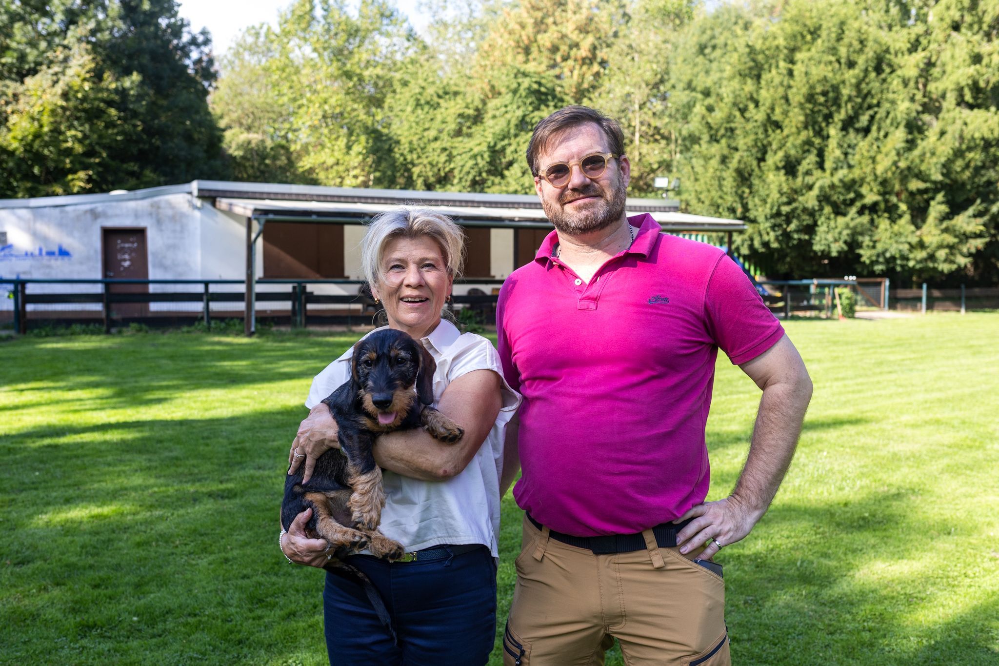 Ein Mann und eine Frau mit Dackel auf dem Arm lachen in die Kamera.