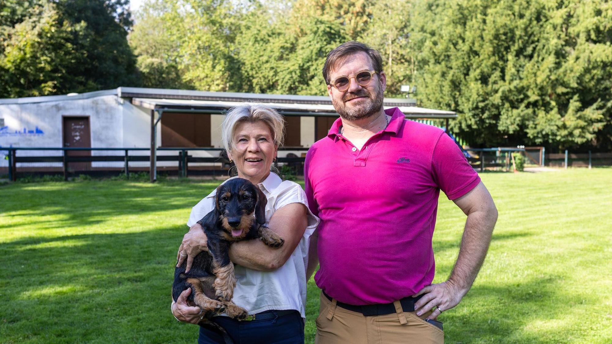 Ein Mann und eine Frau mit Dackel auf dem Arm lachen in die Kamera.