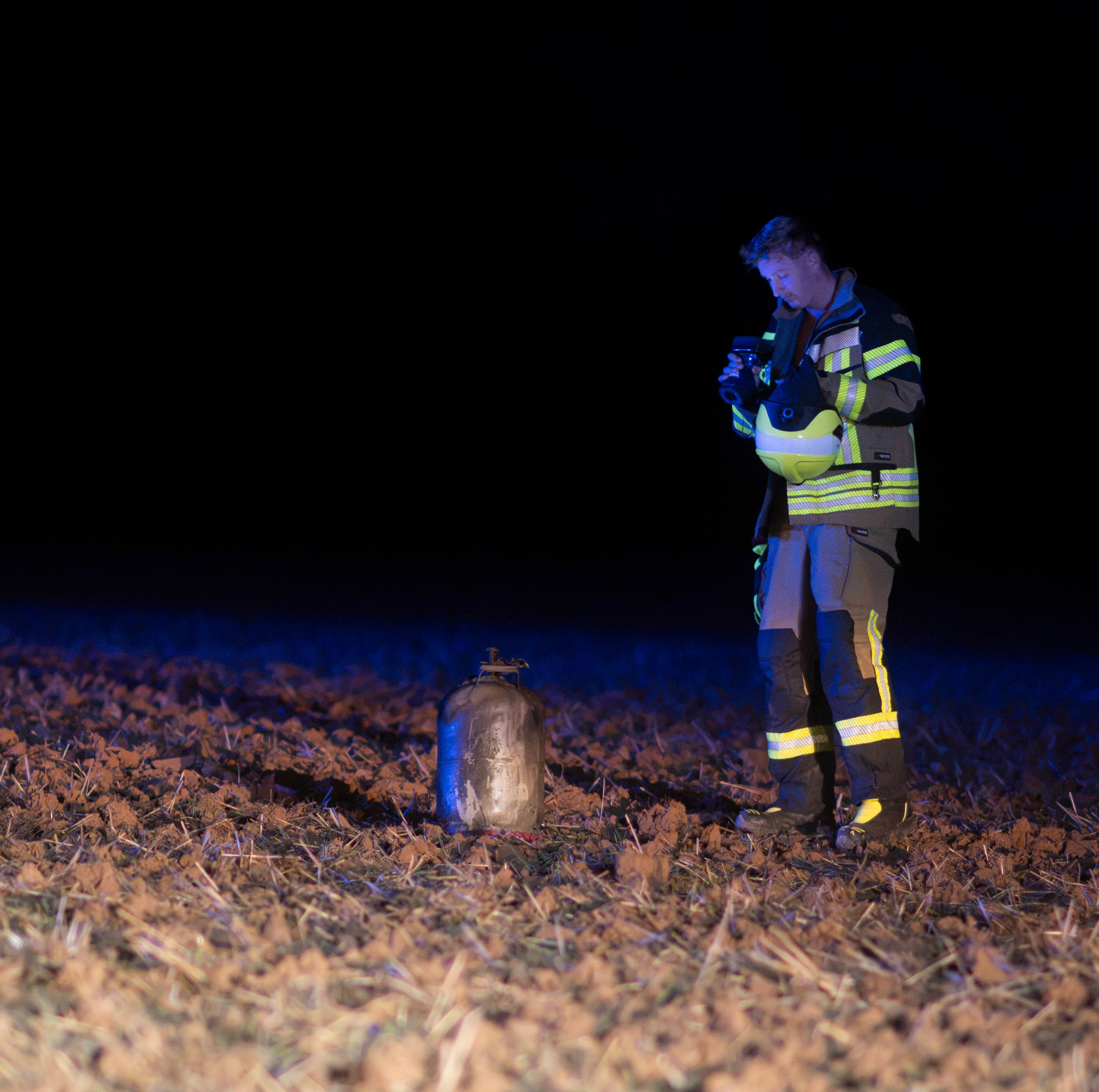 Auf einem Feld steht eine Gasflasche, daneben ein Feuerwehrmann. Das Foto wurde im Dunkeln aufgenommen.