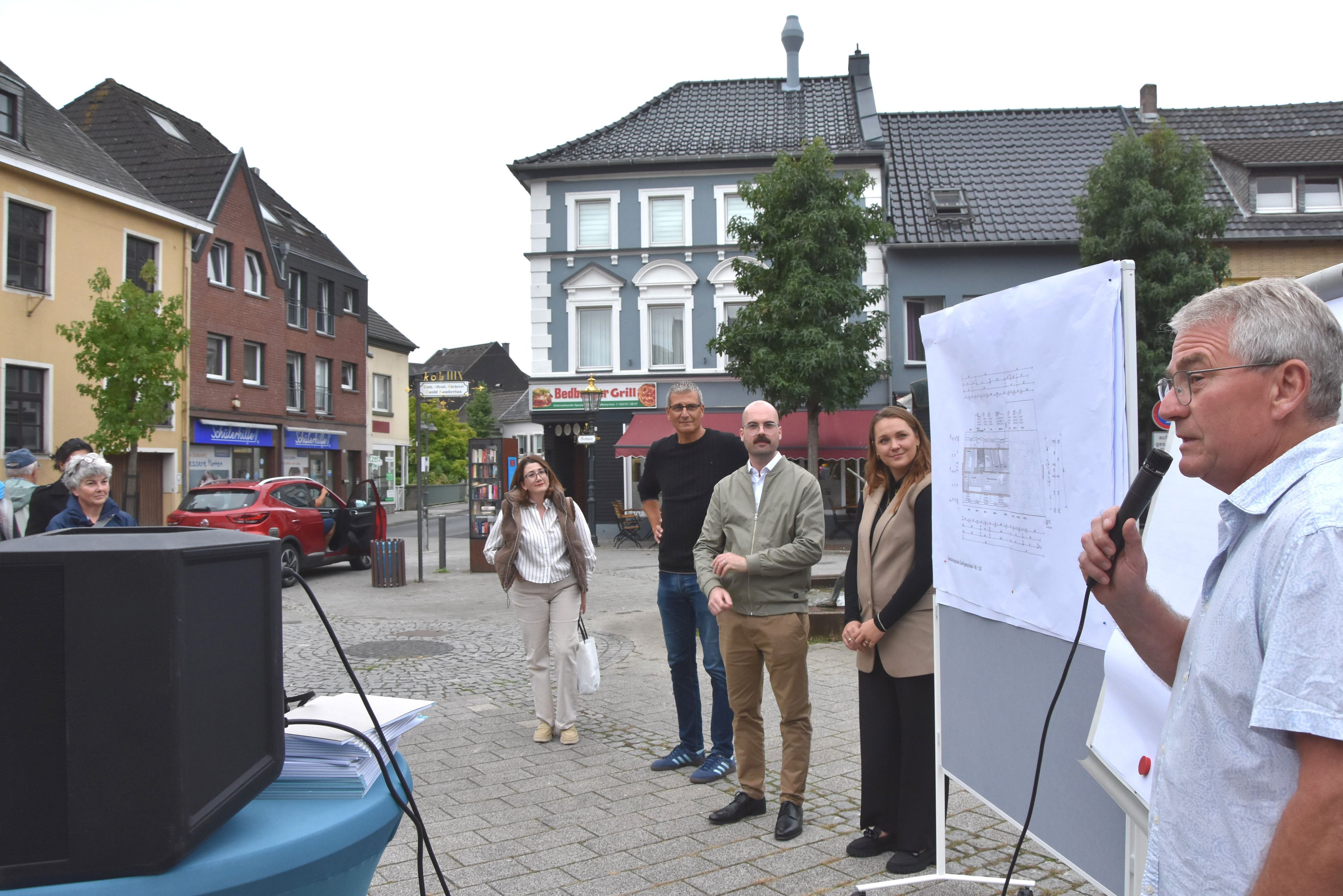 Auf dem Bild ist eine Gruppe von Menschen auf dem Marktplatz zu sehen.
