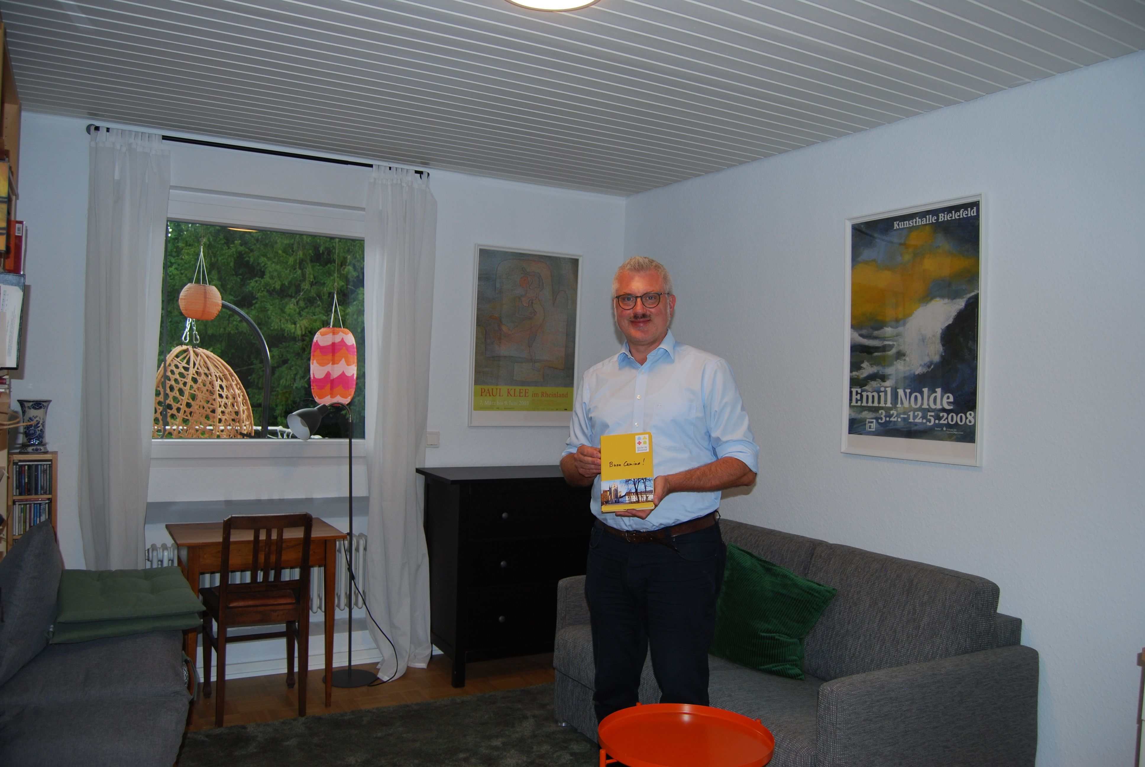 Ein Mann steht vor einem Bettsofa in einem einfach eingerichteten Zimmer