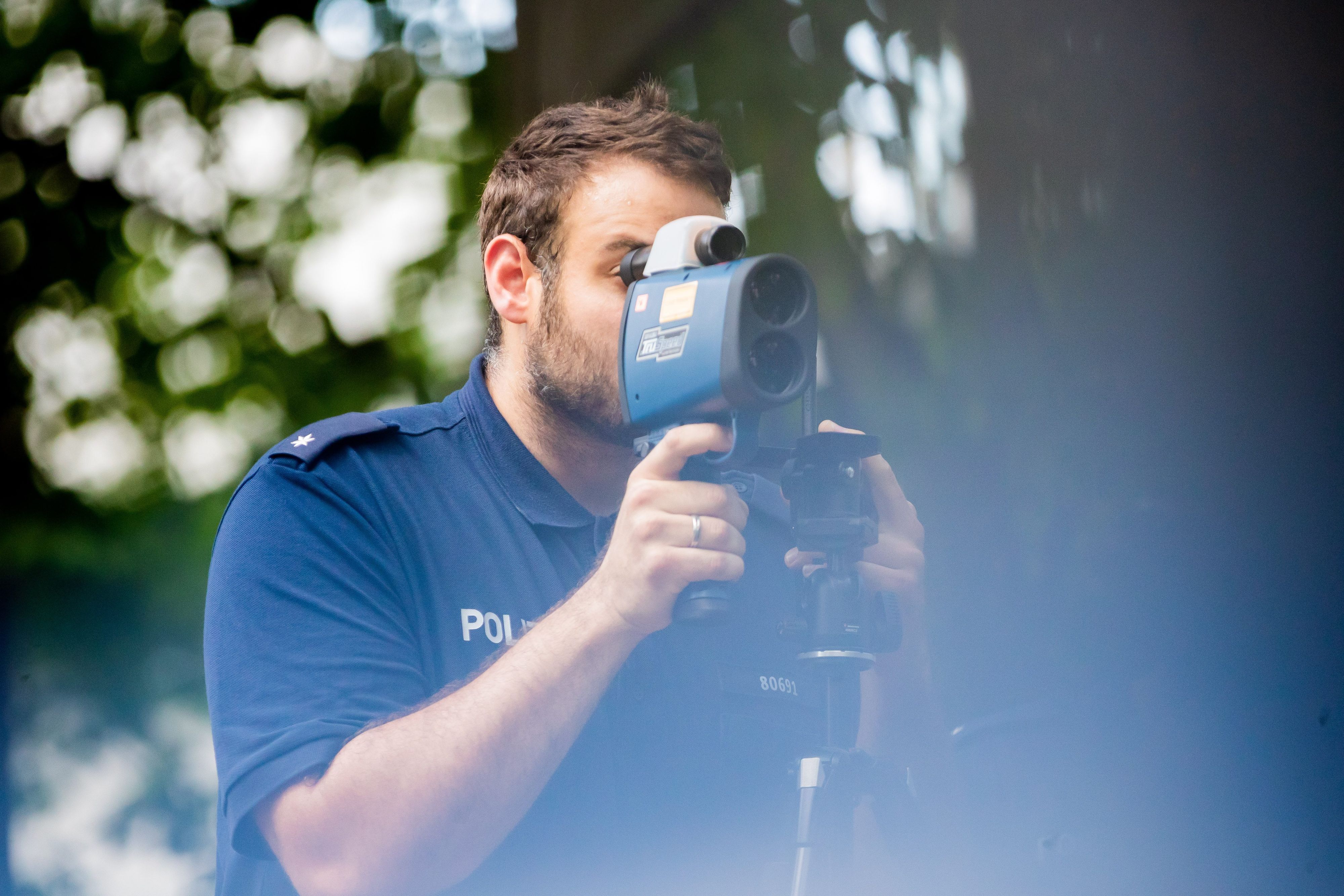 24.08.2022, Berlin: Polizeikommissar Schäfer kontrolliert bei einer Verkehrskontrolle der Berliner Polizei auf der Fulhamer Allee im Berliner Bezirk Neukölln nahe einer Schule mit einem Lasermessgerät die Geschwindigkeit des Autoverkehrs. (zu dpa: "Verkehrssünder bringen Ländern und Kommunen mehr Einnahmen") Foto: Christoph Soeder/dpa +++ dpa-Bildfunk +++