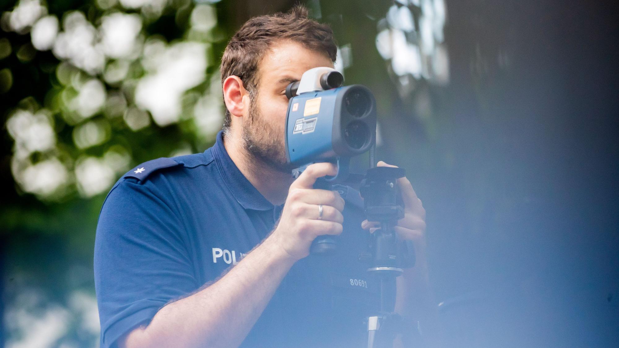 24.08.2022, Berlin: Polizeikommissar Schäfer kontrolliert bei einer Verkehrskontrolle der Berliner Polizei auf der Fulhamer Allee im Berliner Bezirk Neukölln nahe einer Schule mit einem Lasermessgerät die Geschwindigkeit des Autoverkehrs. (zu dpa: "Verkehrssünder bringen Ländern und Kommunen mehr Einnahmen") Foto: Christoph Soeder/dpa +++ dpa-Bildfunk +++