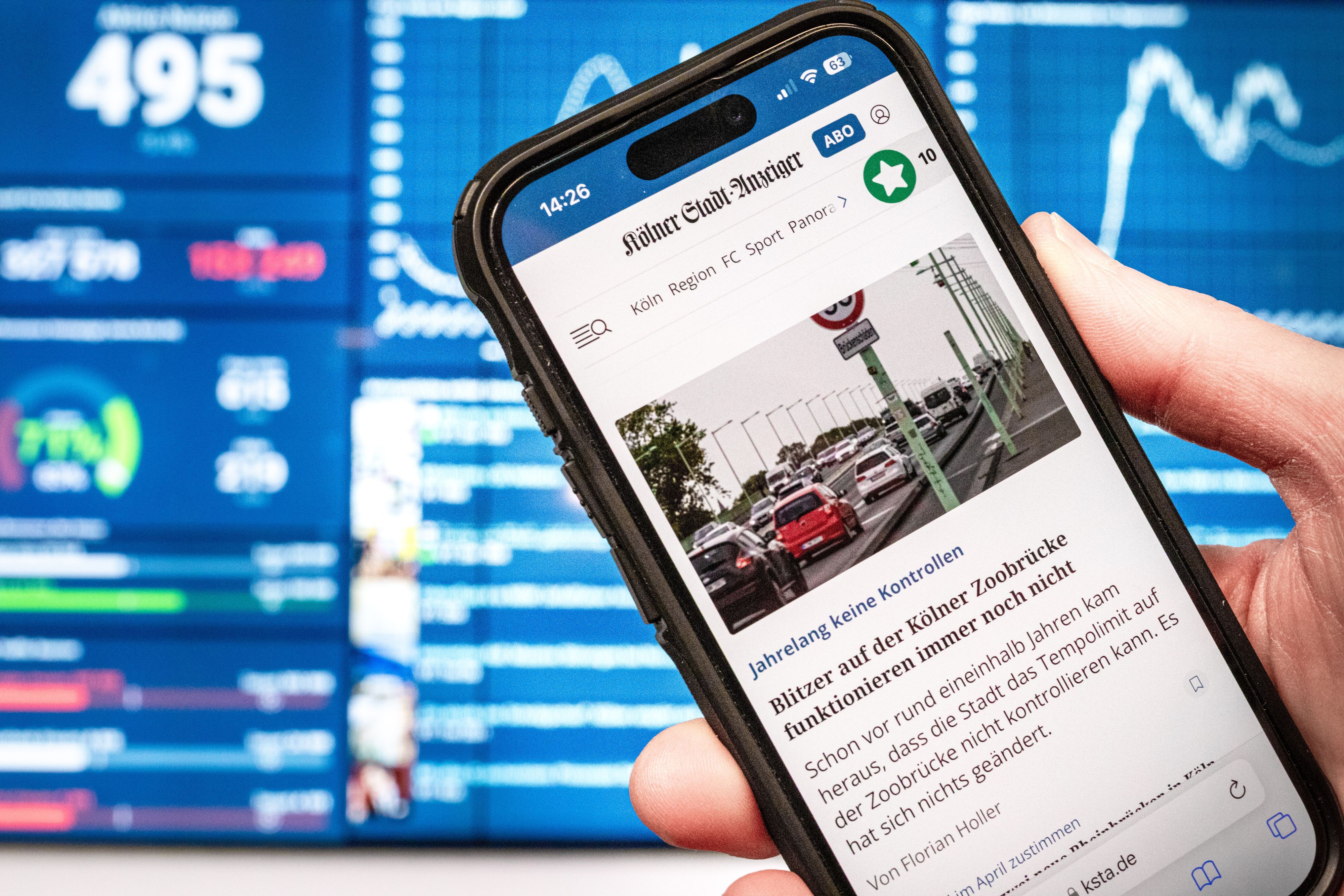 13.02.2025, Köln: Die Webseite des Kölner Stadt-Anzeigers ksta.de ist auf einem Smartphone zu sehen. Im Hintergrund ist ein Monitor im Newsroom der Tageszeitung sichtbar. Foto: Matthias Heinekamp