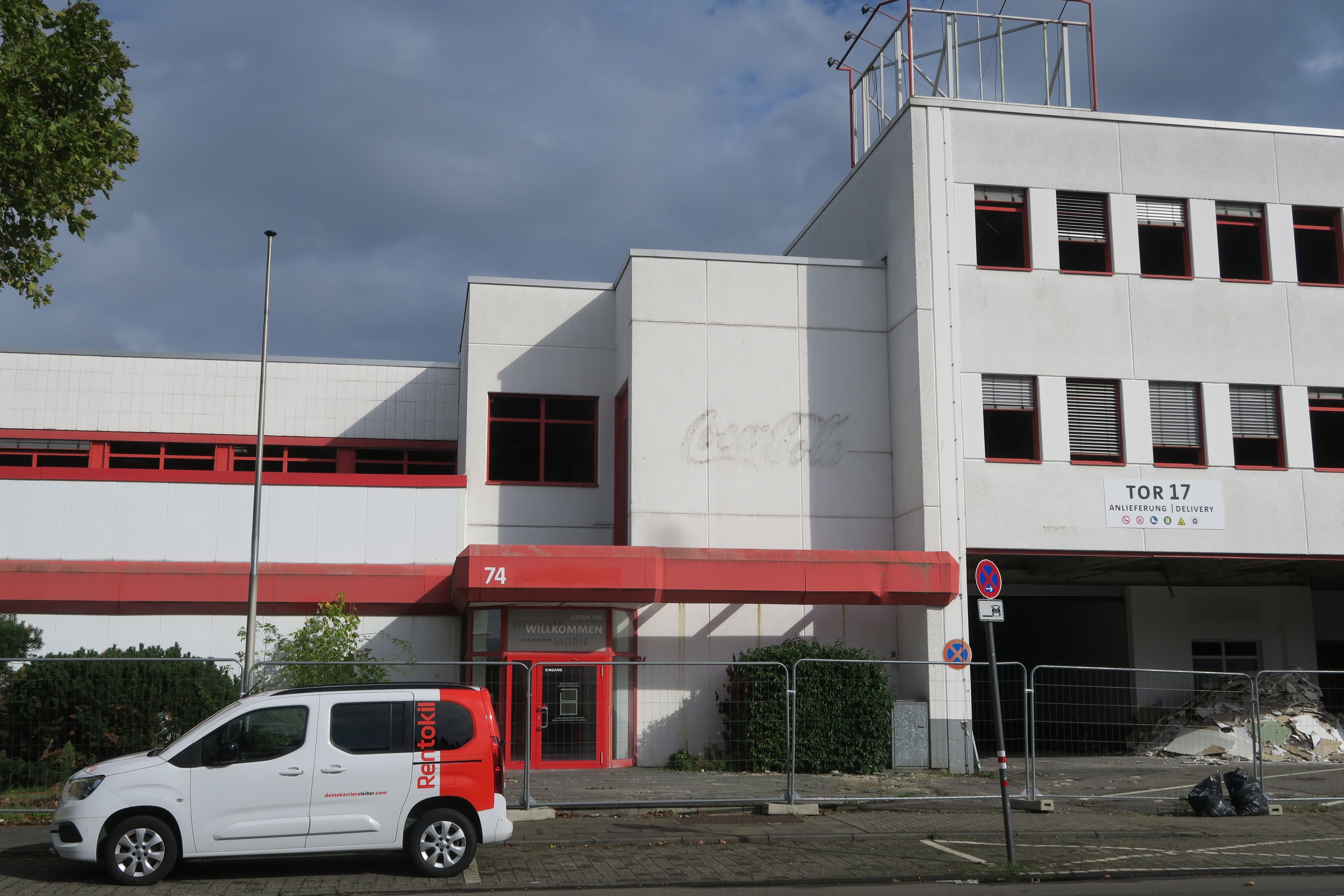 Vor einem dreistöckigen Bürogebäude parkt ein weiß-roter Kleintransporter.