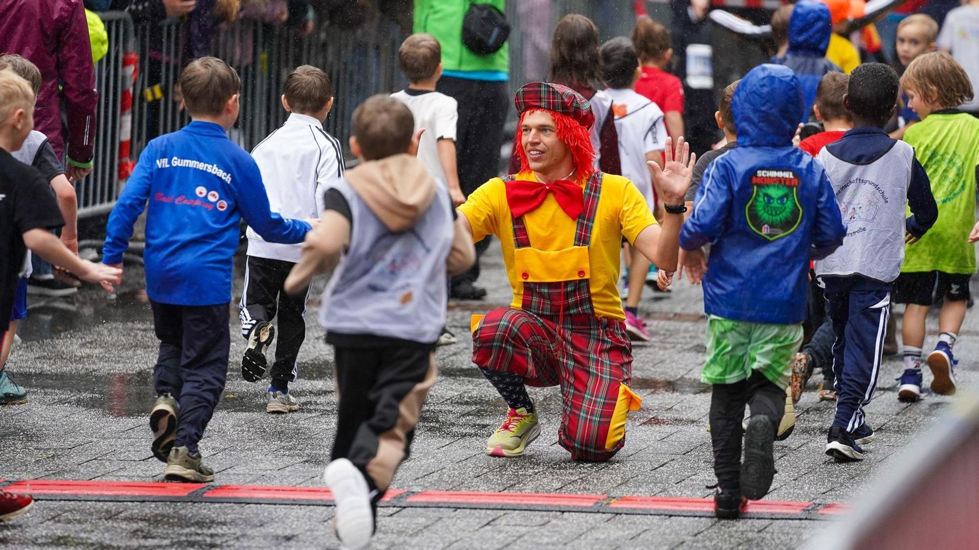 Der Laufclown kniet im Ziel und klatscht die Kinder ab.
