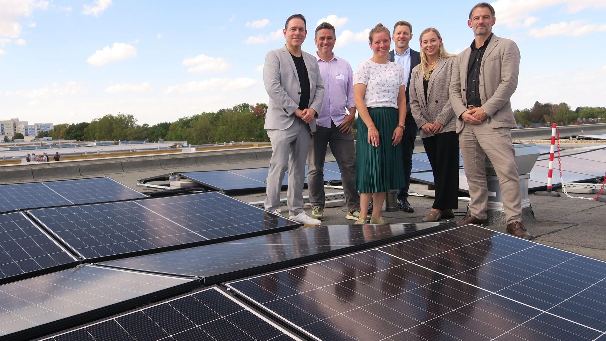 Vier Männer und zwei Frauen stehen neben Solarpaneelen auf einem Flachdach.