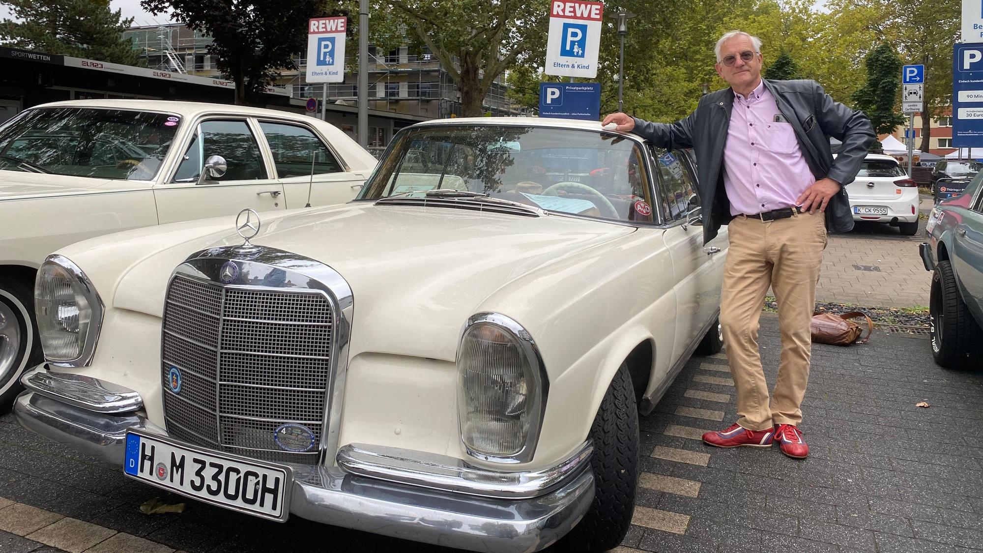 Ein Mann lehnt sich an ein cremefarbenes Mercedes-Coupé.