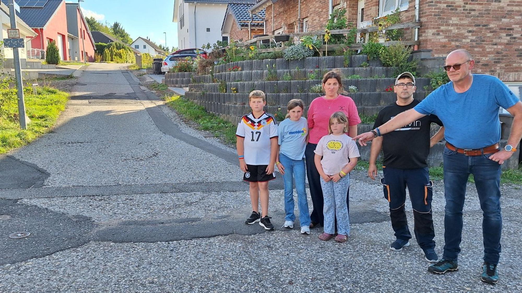 Die genannten Personen stehen an einer Erschließungsstraße in einem Neubaugebiet, Matthias Stegemann deutet auf Schäden der groben Asphaltdecke.