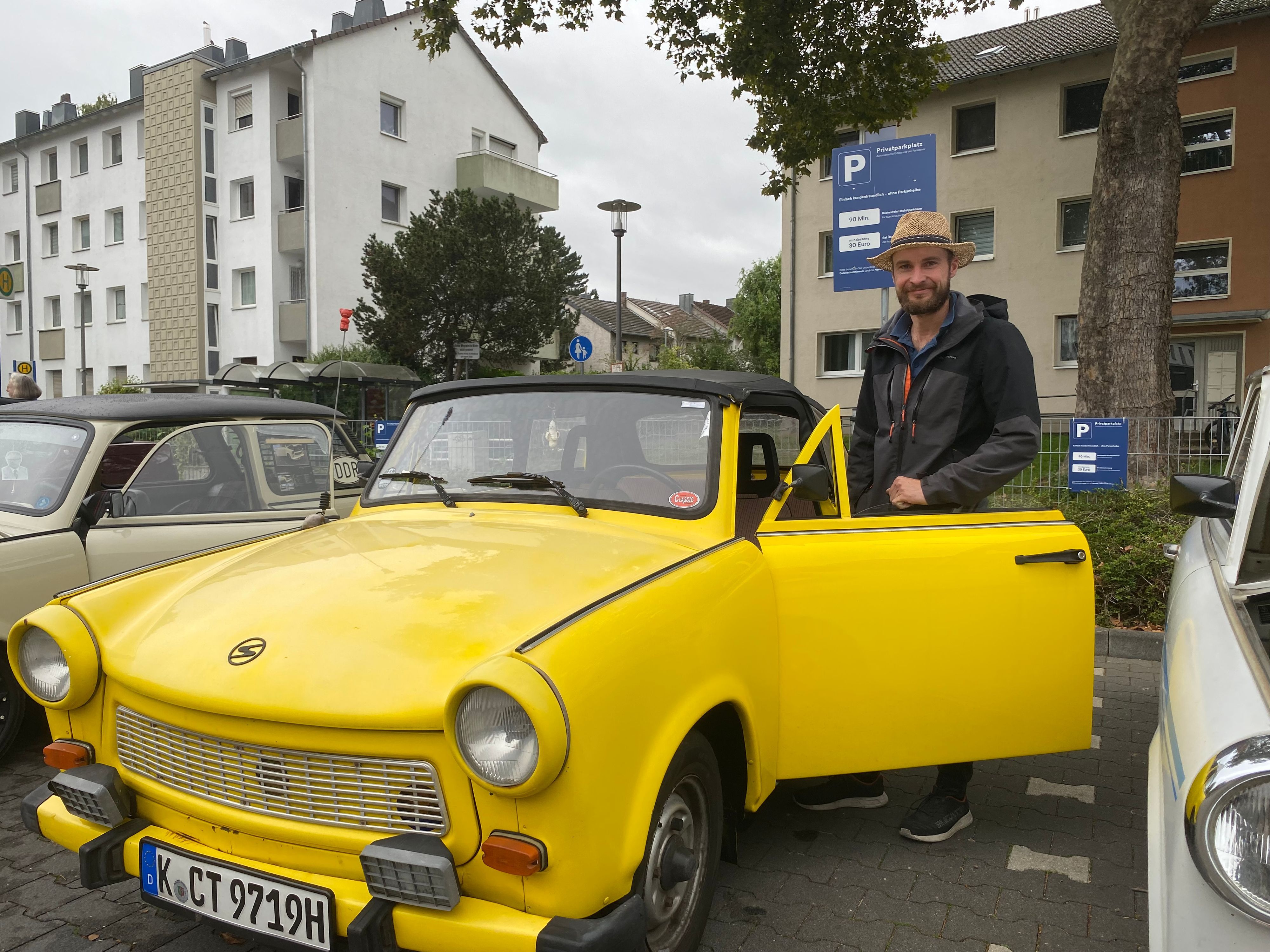 Ein Mann steht hinter einer geöffneten Tür eines gelbfarbenen Trabants.