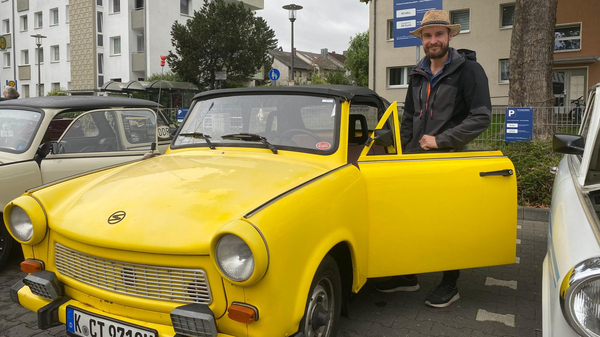 Ein Mann steht hinter einer geöffneten Tür eines gelbfarbenen Trabants.