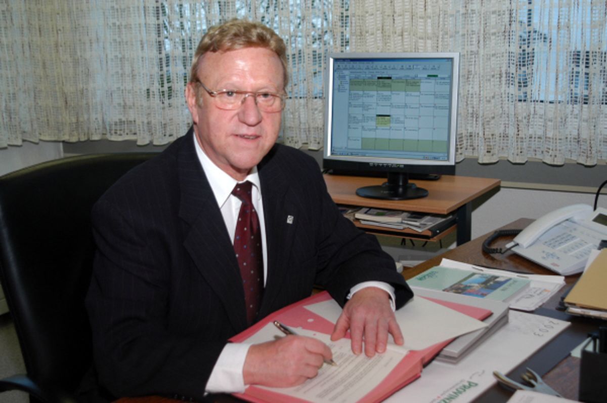 Hans Kaiser sitzt an seinem Schreibtisch, einen Stift und Unterlagen vor sich liegend.