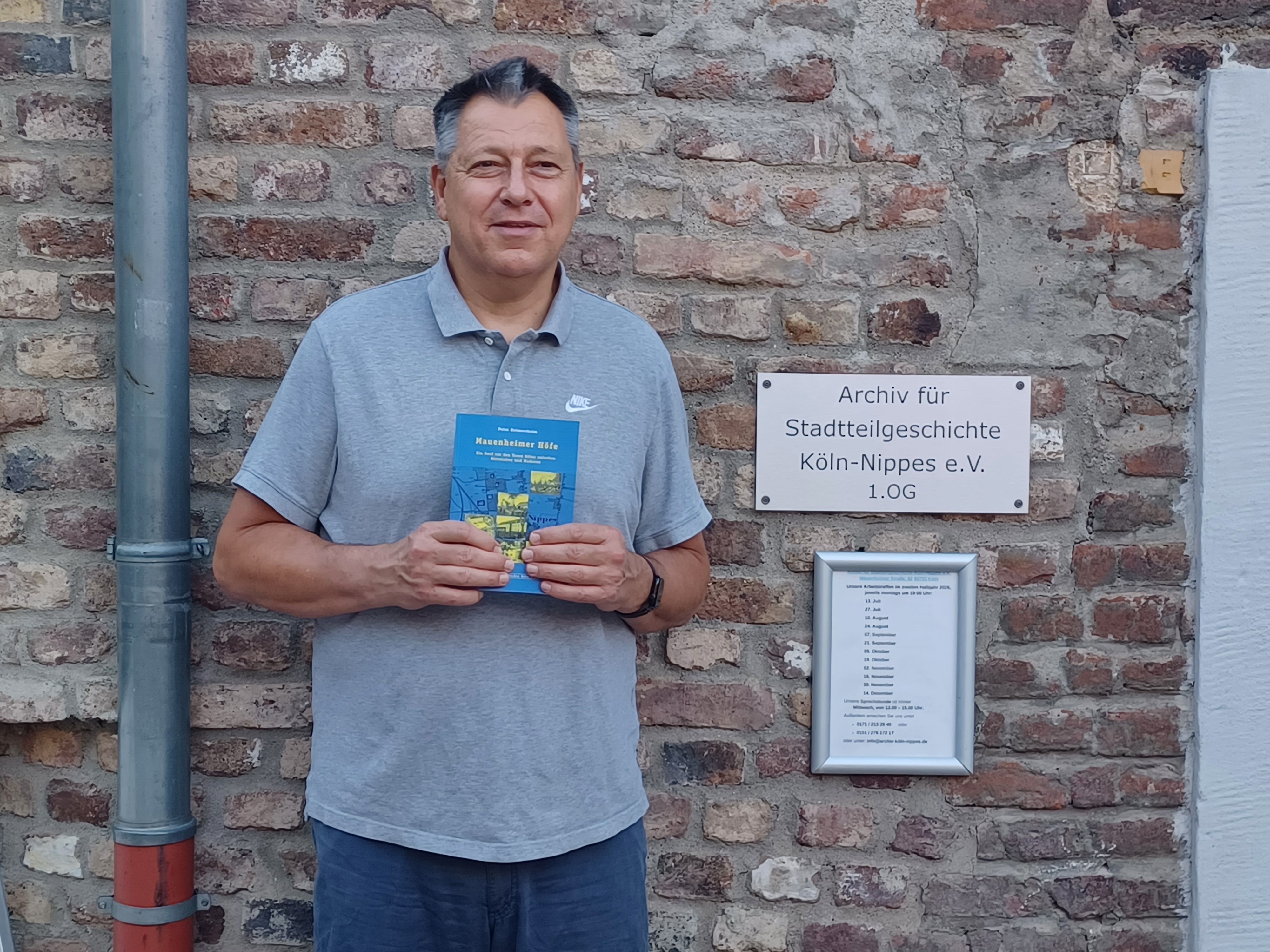Peter Heimerzheim mit seinem Buch, vor dem Eingang des Stadtteilarchivs im Bürgerzentrum Altenberger Hof.