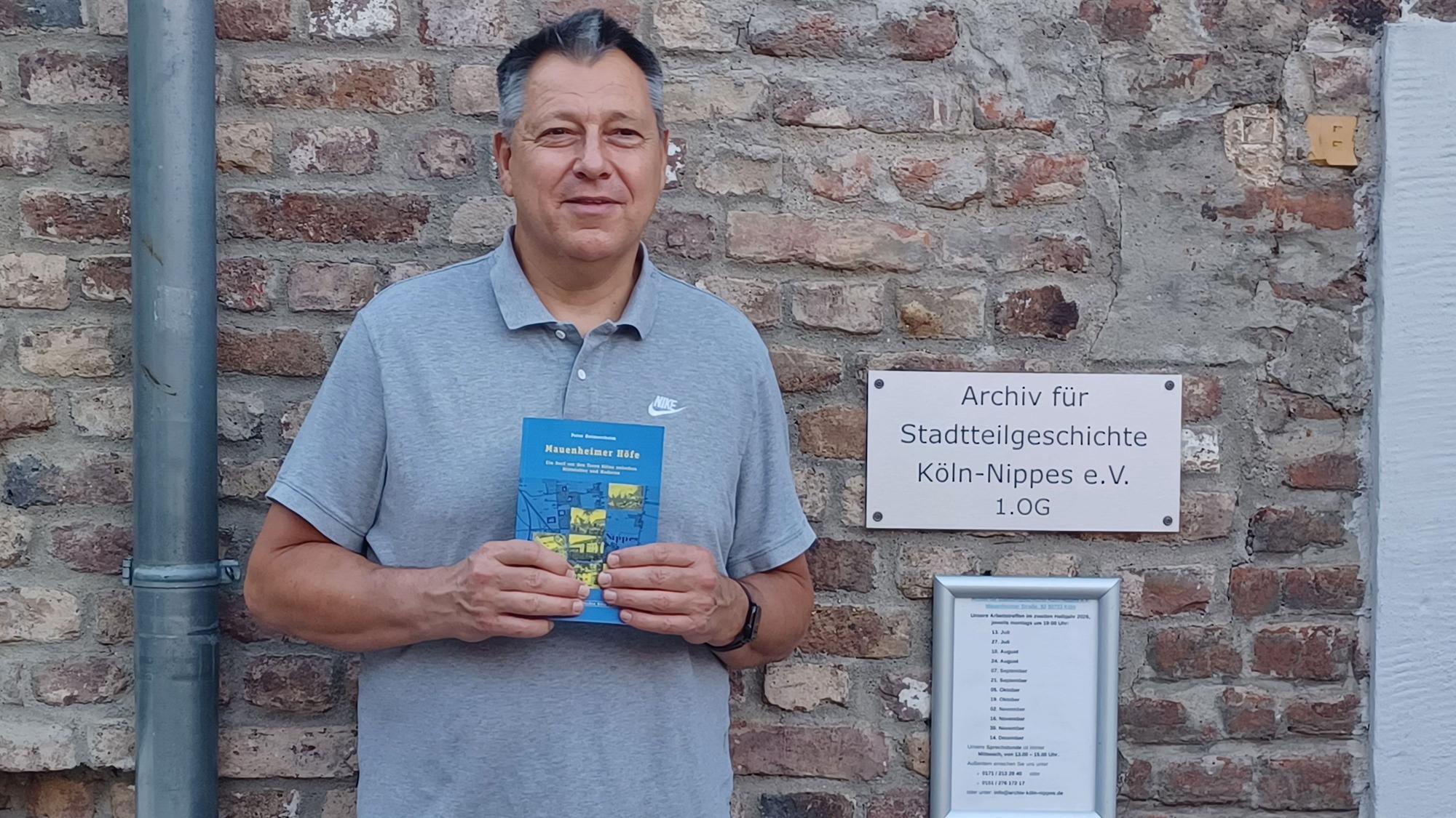 Peter Heimerzheim mit seinem Buch, vor dem Eingang des Stadtteilarchivs im Bürgerzentrum Altenberger Hof.