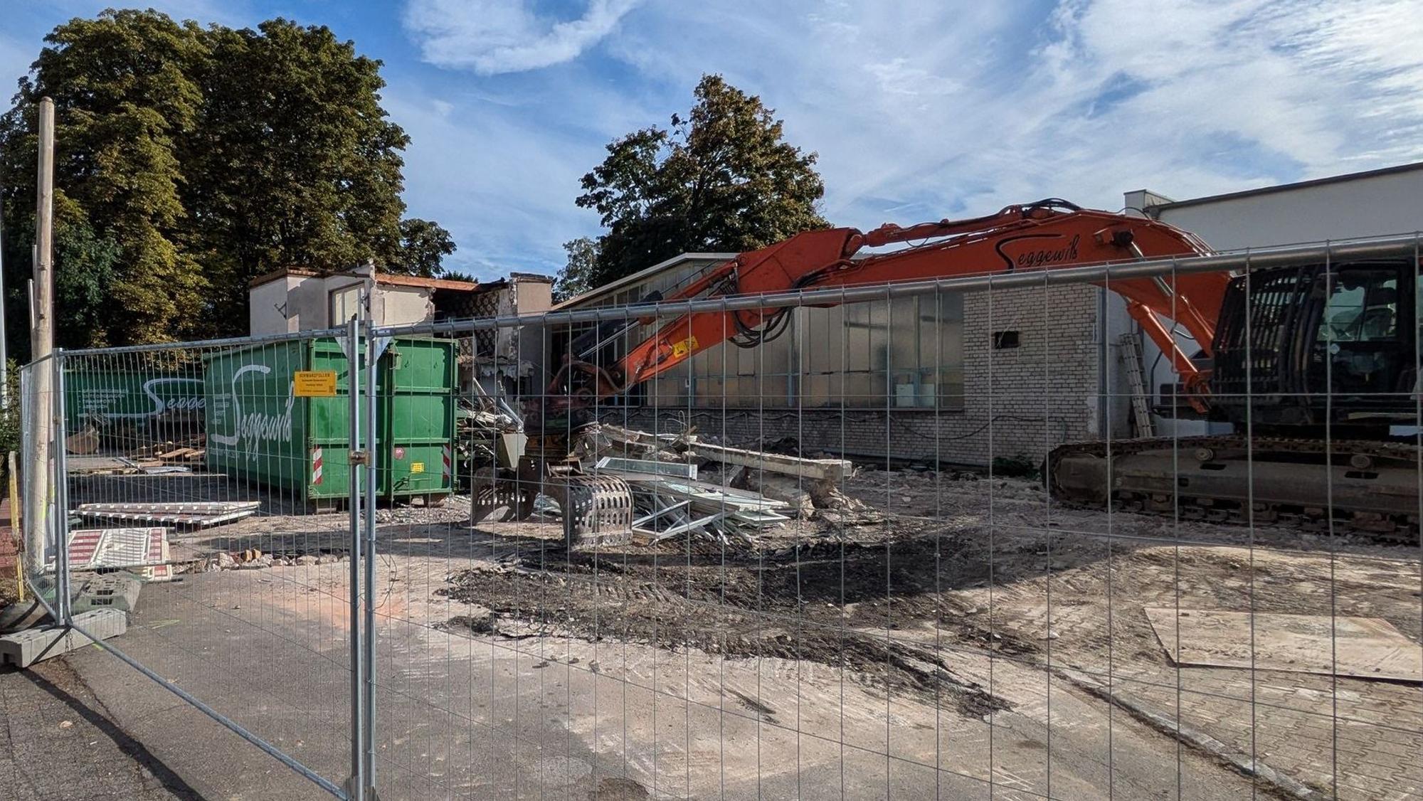 Ein Abrissbagger steht hinter Zäunen.