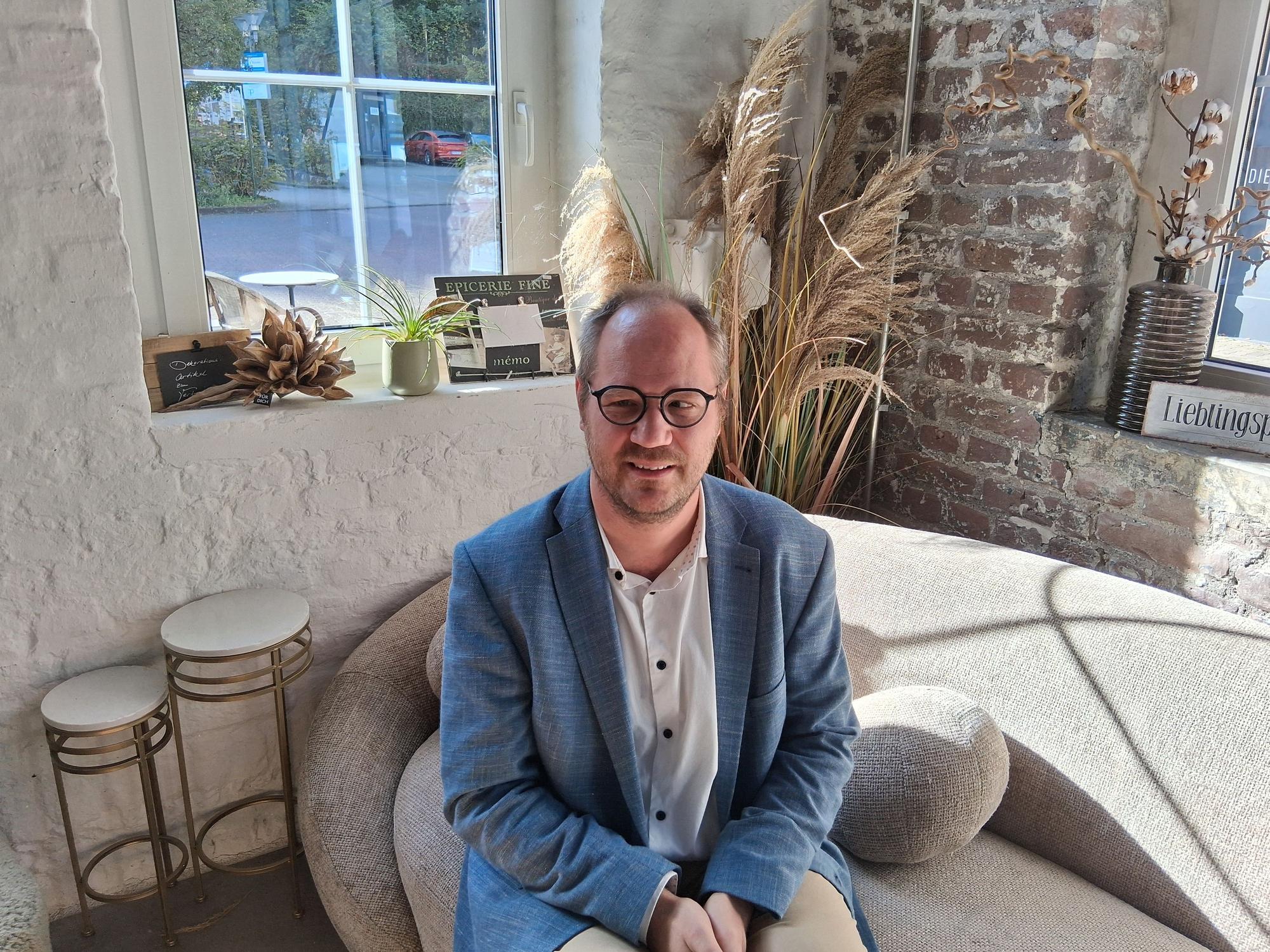 Zu sehen ist ein lächelnder Mann in einem Café.