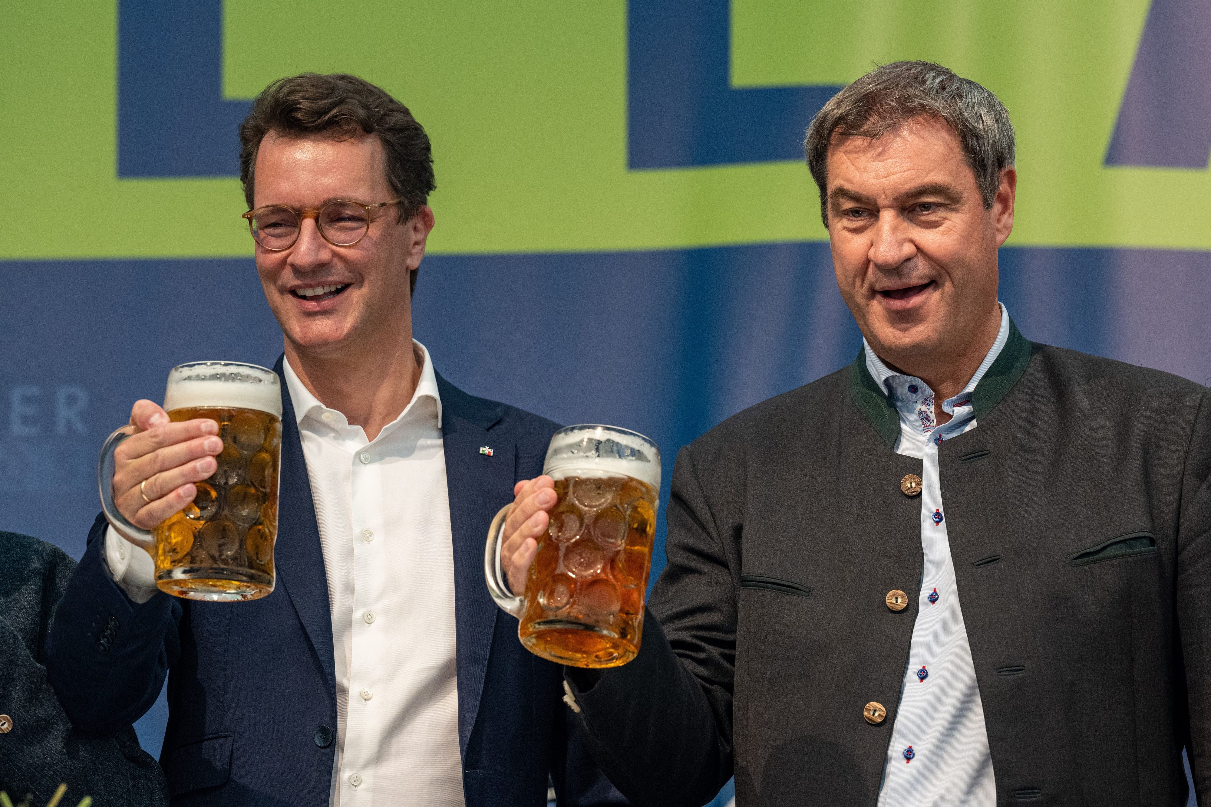 Markus Söder (r), Bayerns Ministerpräsident und CSU-Parteichef, und Hendrik Wüst, NRW-Ministerpräsident (CDU), stehen bei einem Volksfest mit Bierkrügen auf der Bühne.