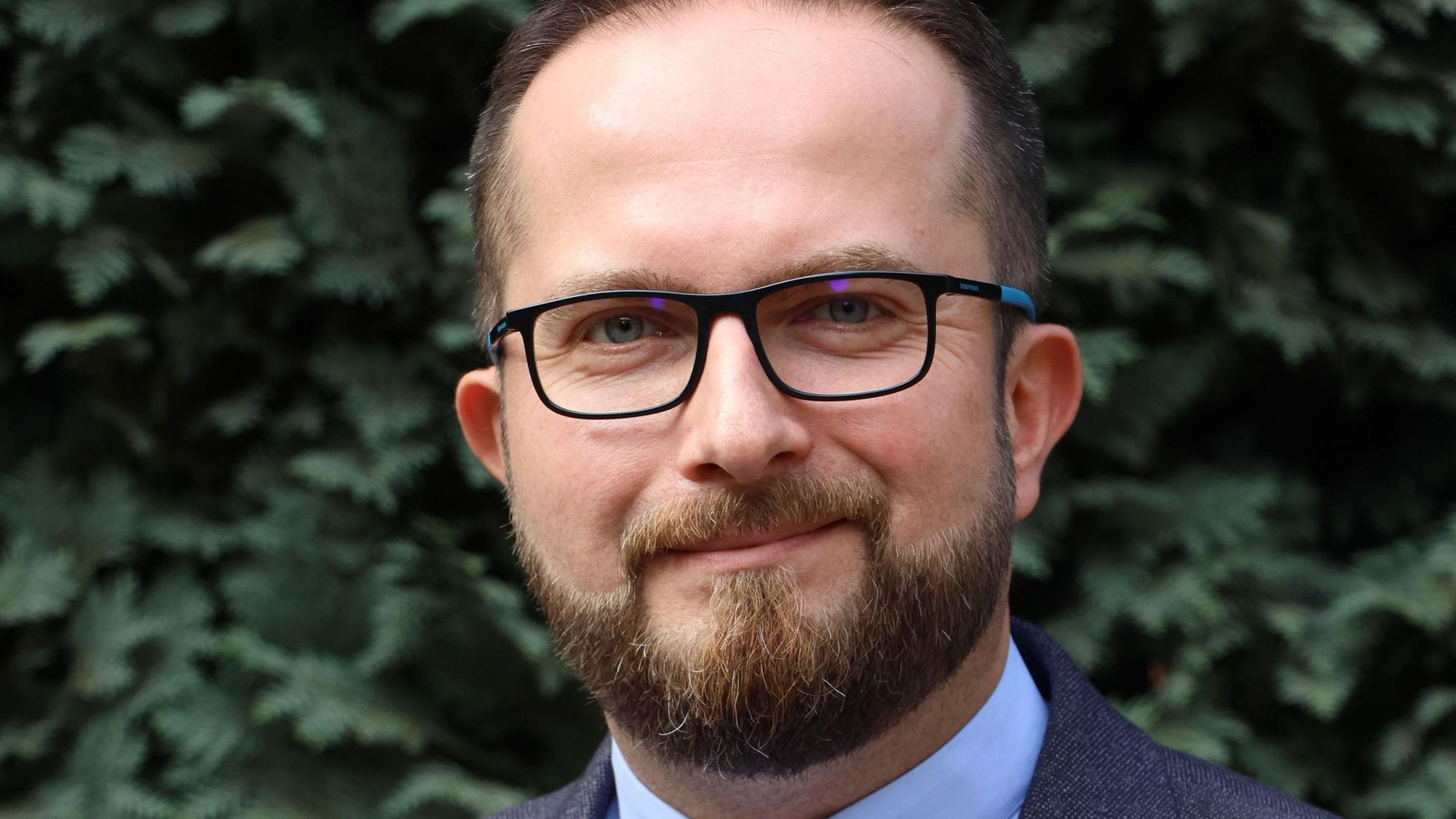 Ein Mann mit Bart und Brille lächelt in die Kamera.