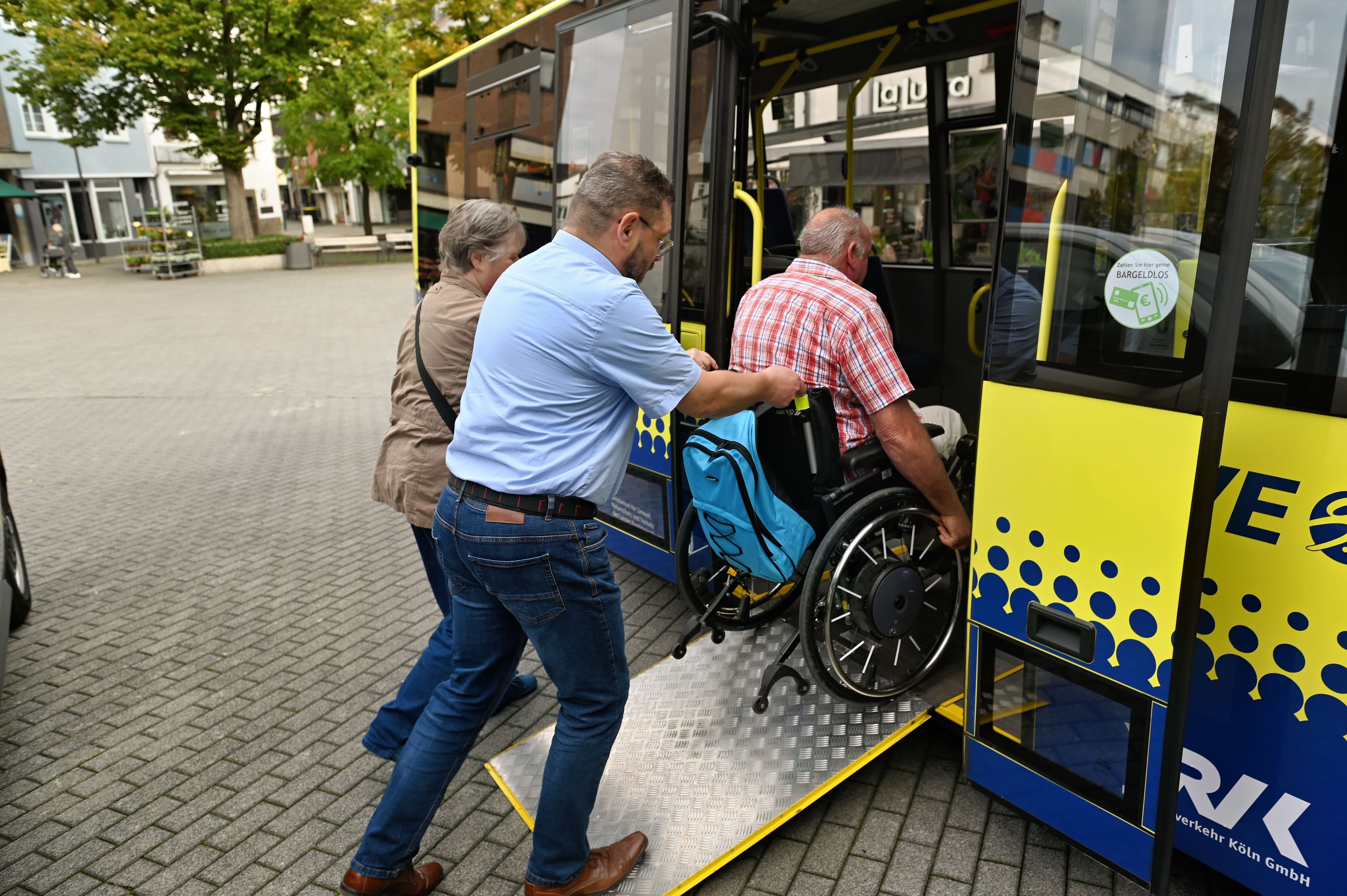 Zwei Leute schieben einen Rollstuhl über eine Rampe in den Bus.