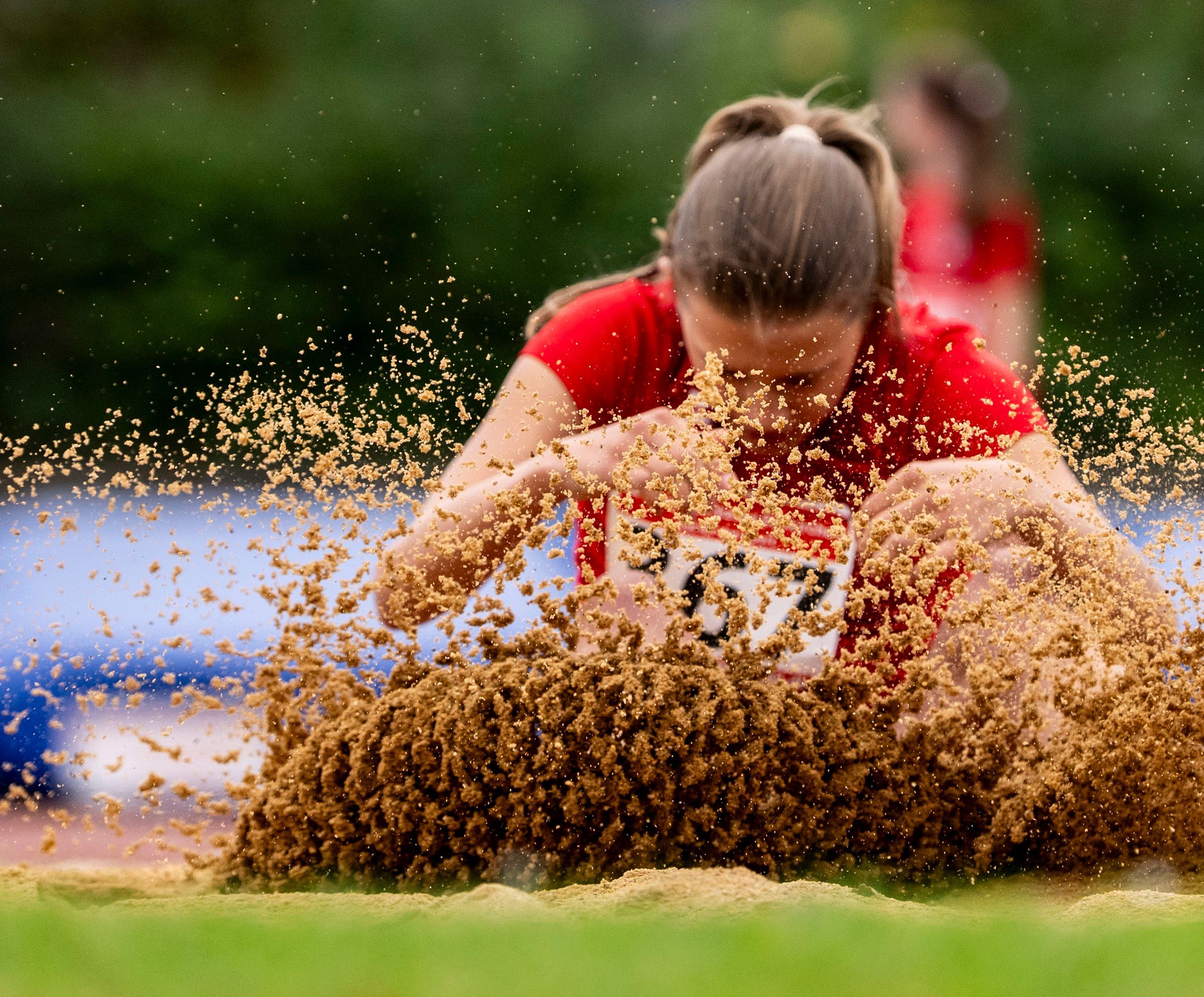 Eine Weitspringerin landet in der Grube. Der Sand spritzt.