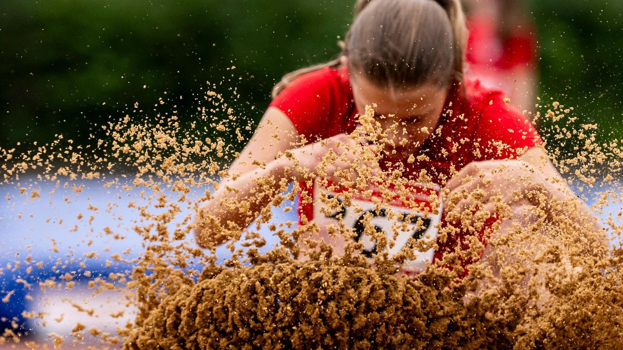 Eine Weitspringerin landet in der Grube. Der Sand spritzt.