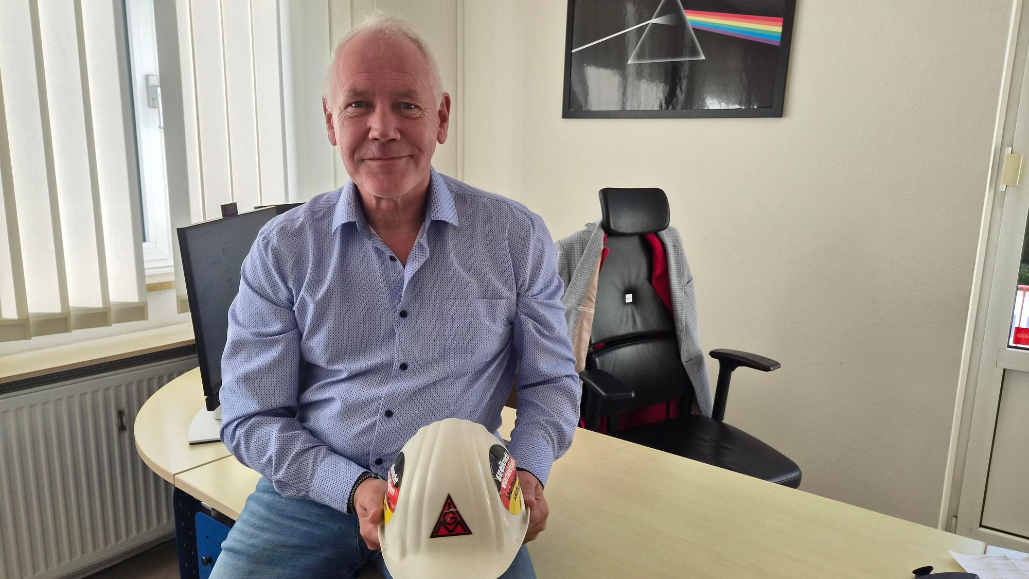 Ein Mann sitzt am Schreibtisch und hält einen Helm in der Hand.