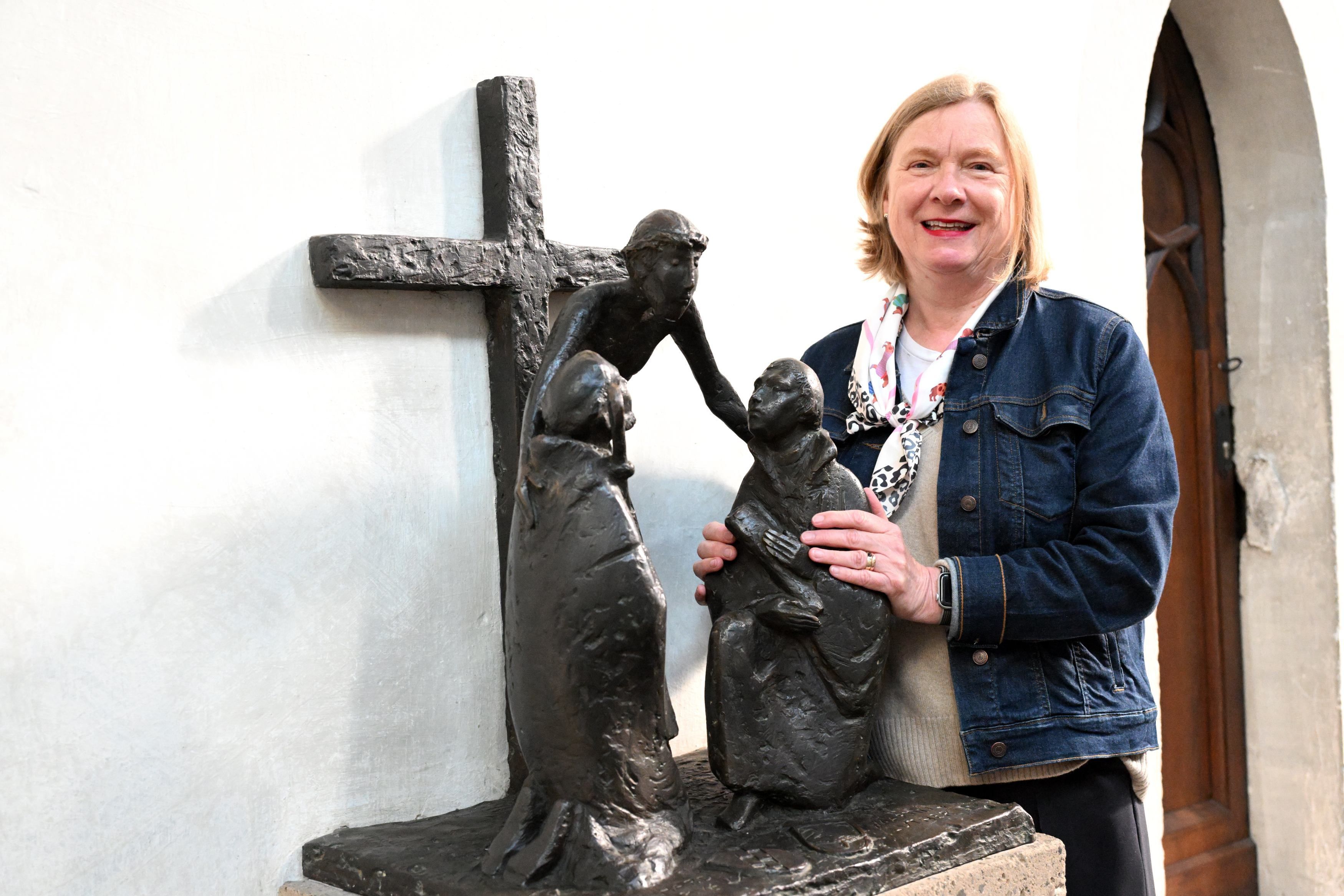 Eine blonde Frau in Jeansjacke steht an einer Bronzeplastik, die Martin Luther zeigt.