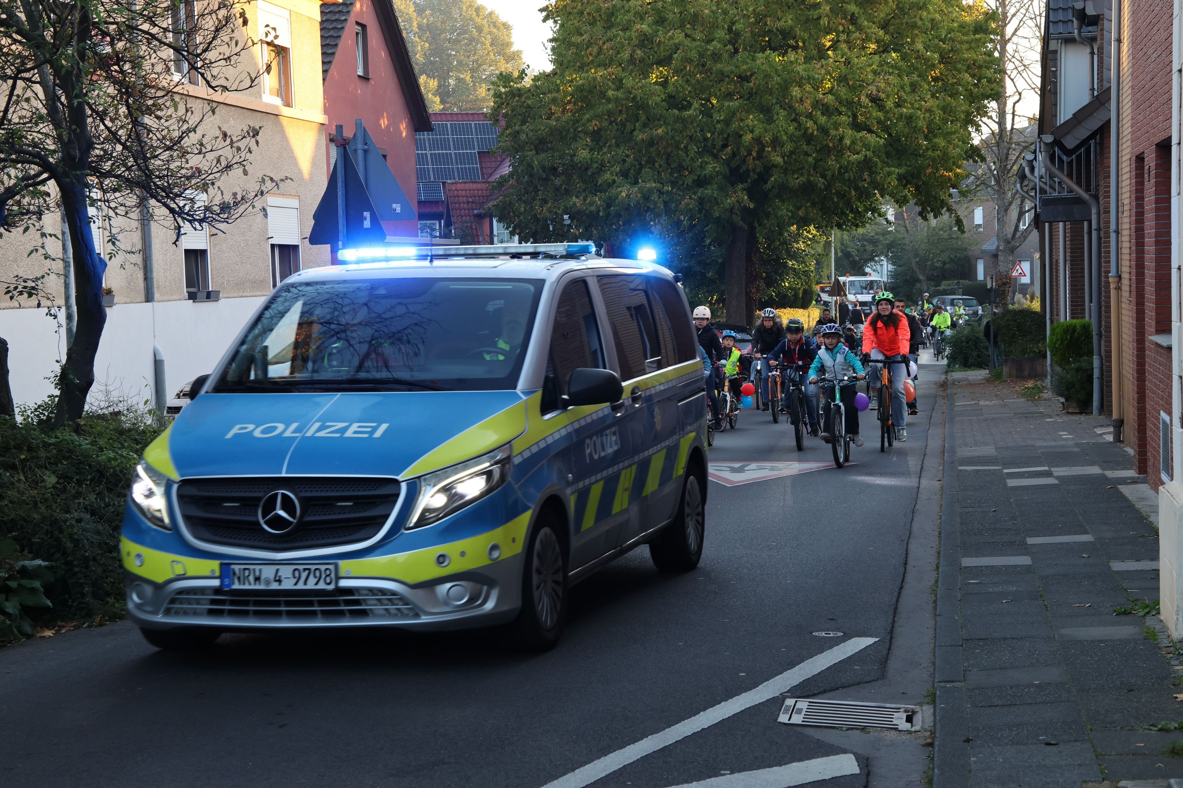 Auf dem Bild ist ein Polizeiauto zu sehen, hinter dem Kinder und Eltern radeln.