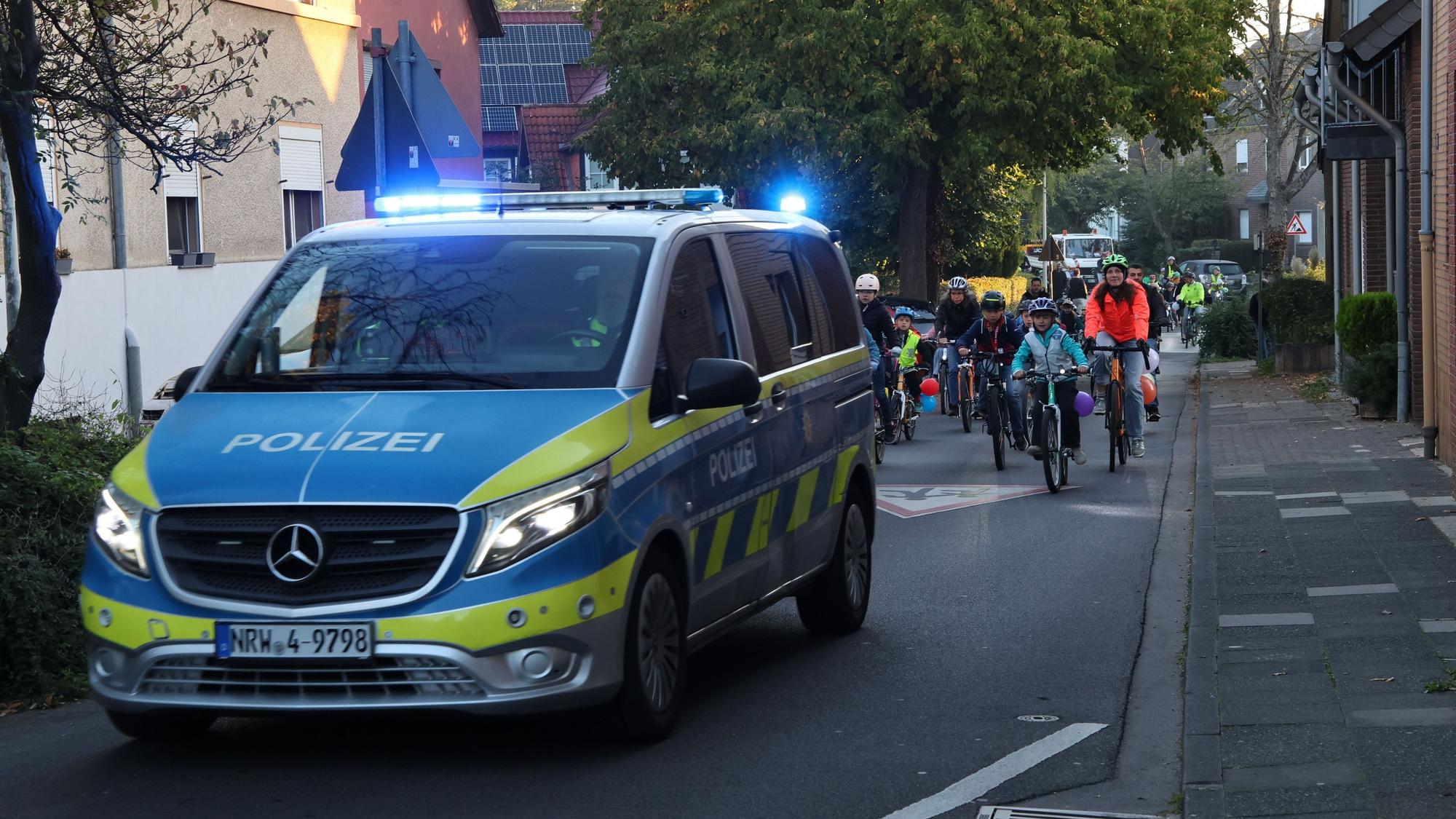 Auf dem Bild ist ein Polizeiauto zu sehen, hinter dem Kinder und Eltern radeln.