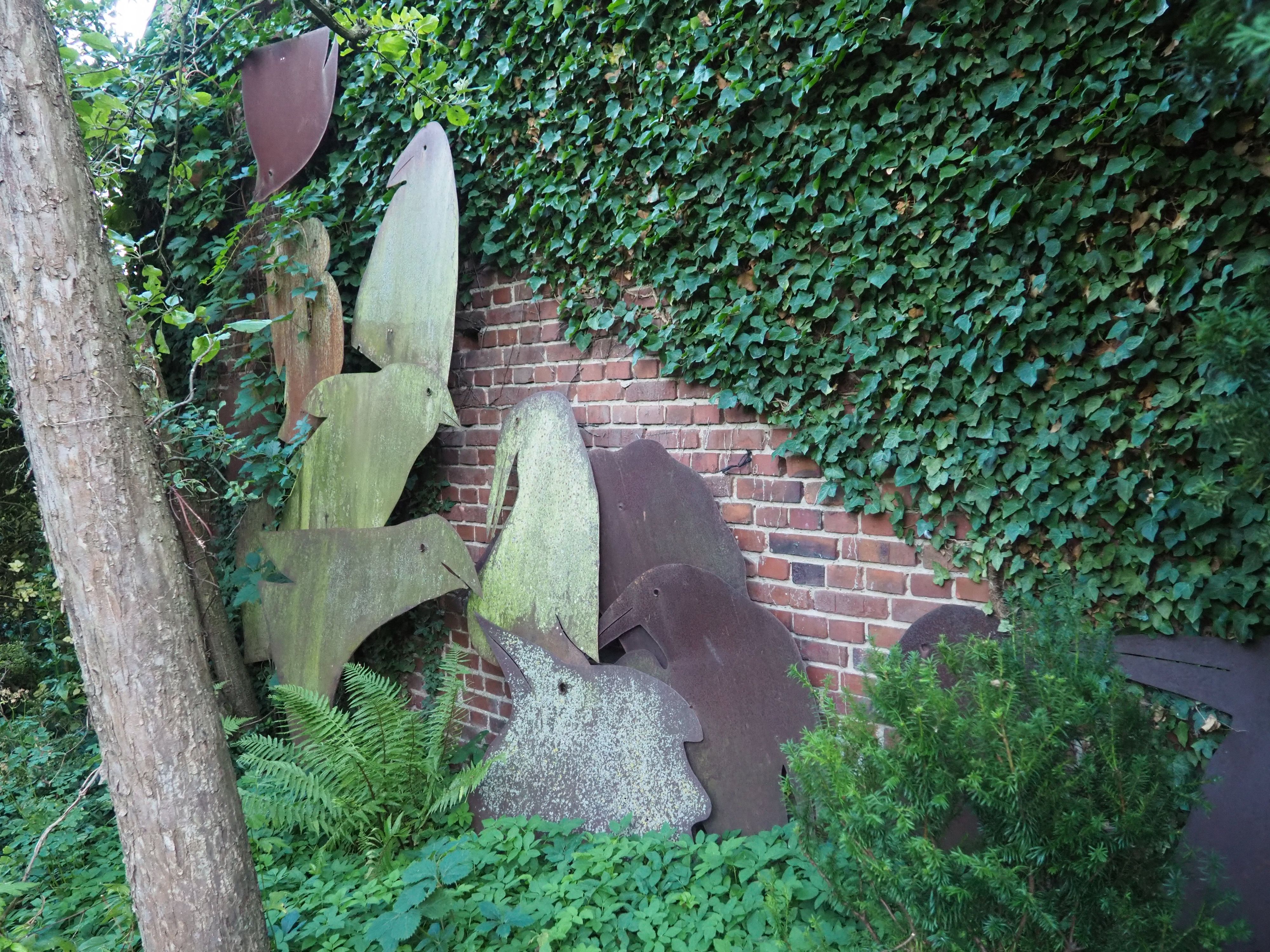 Vor der überwucherten Gartenmauer sind Vogelsilhouetten aufgestellt.