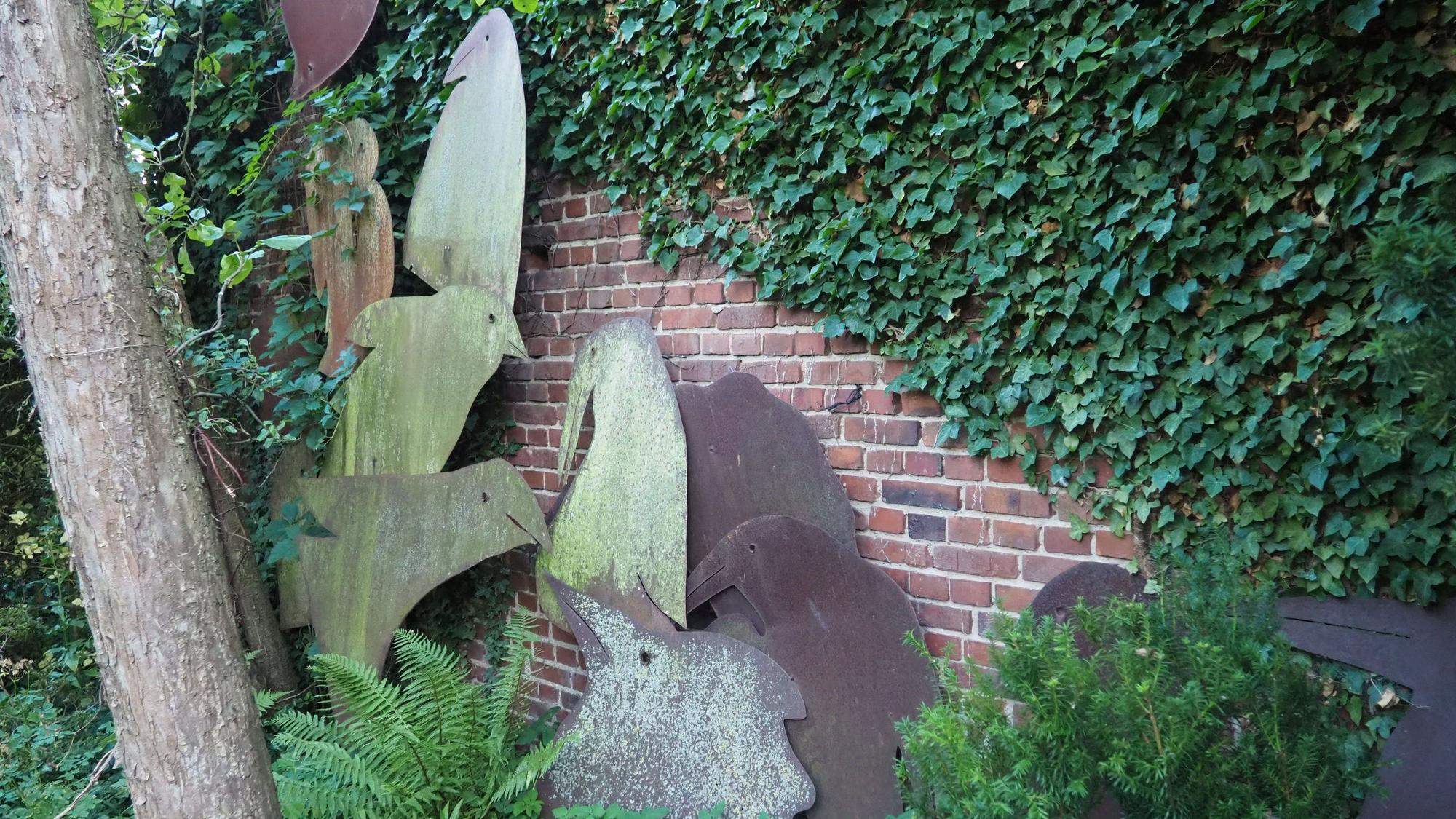 Vor der überwucherten Gartenmauer sind Vogelsilhouetten aufgestellt.