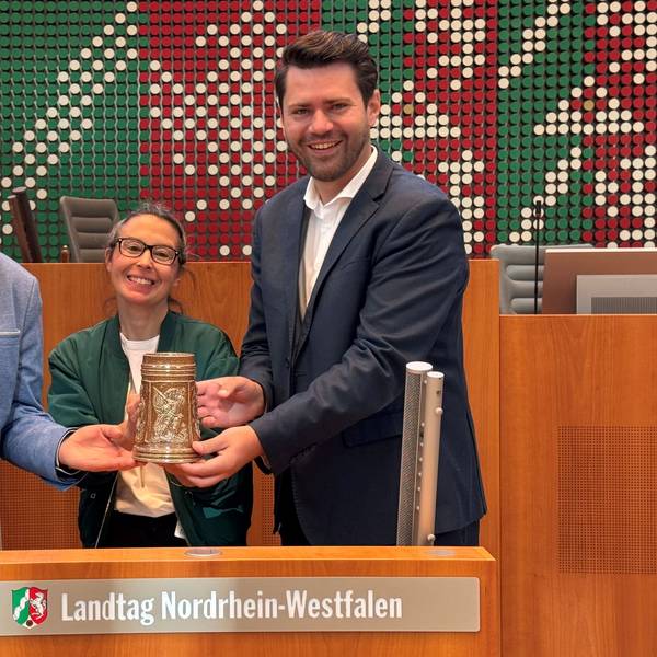 Auf dem Bild sind zwei Männer und eine Frau im Landtag NRW zu sehen.