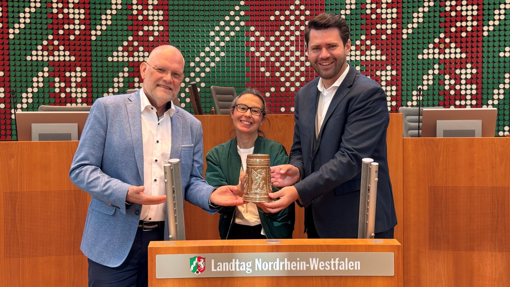 Auf dem Bild sind zwei Männer und eine Frau im Landtag NRW zu sehen.