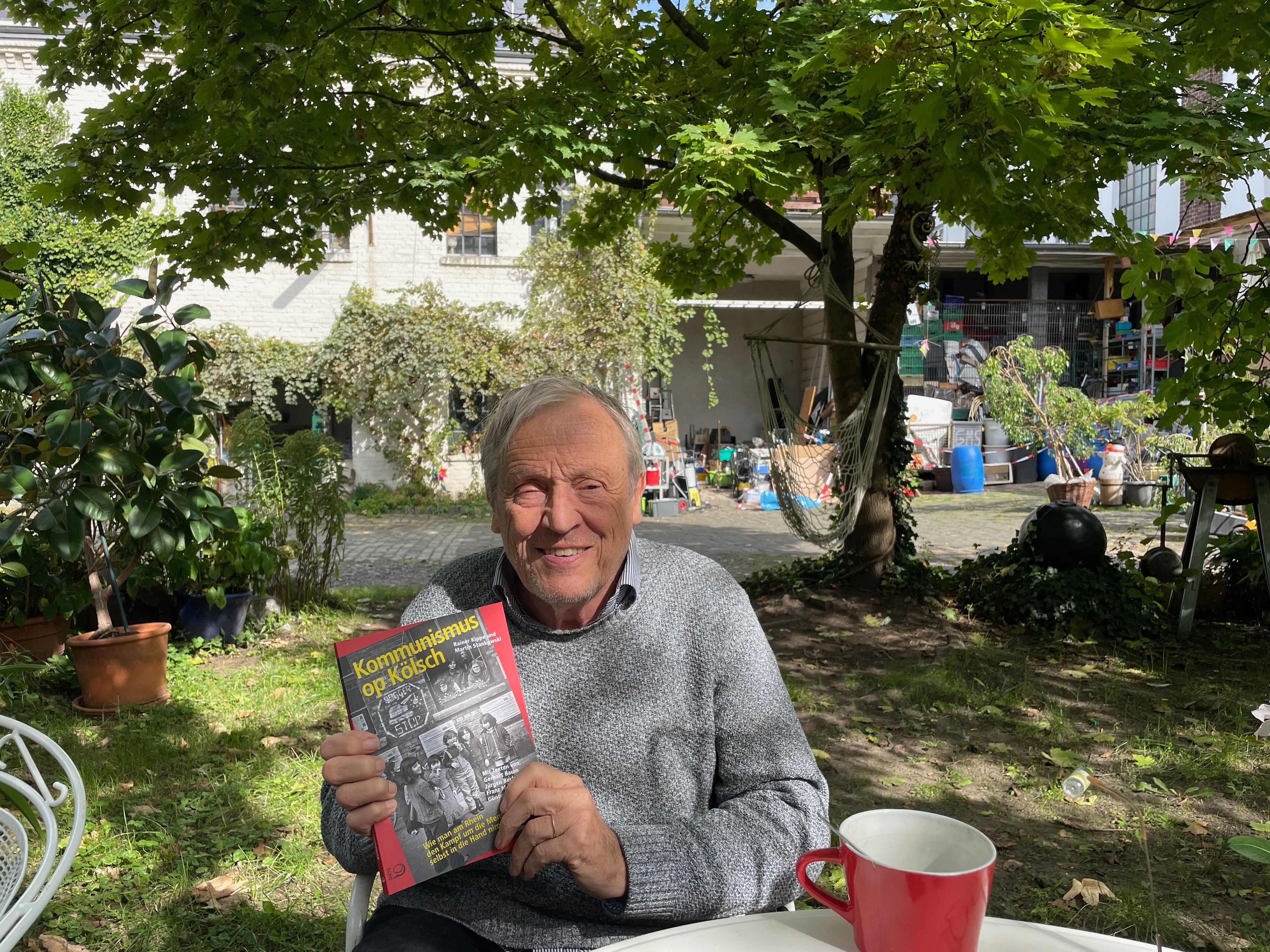 Ein älterer Mann sitzt im Garten, in den Händen hält er ein Buch.