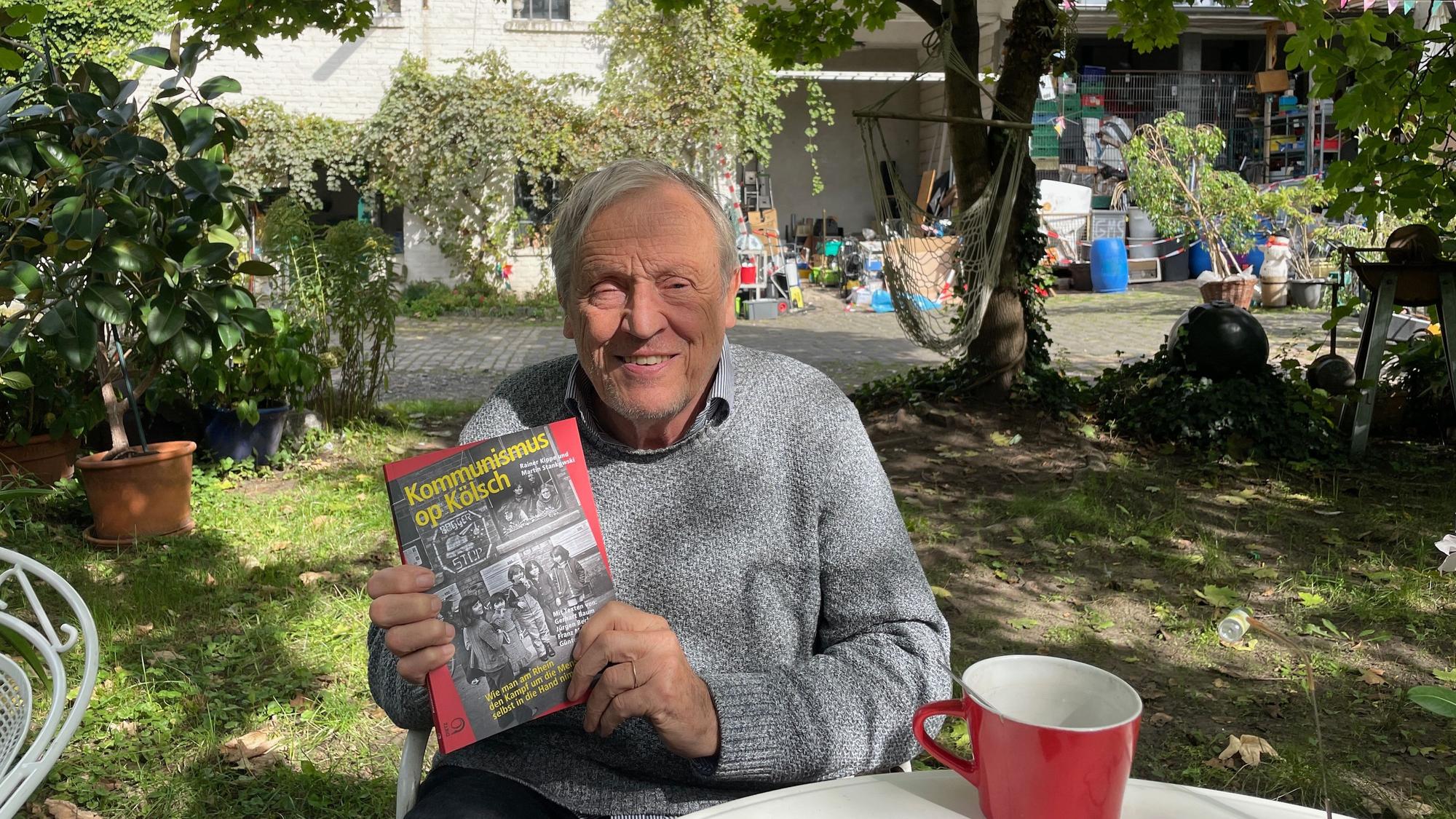 Ein älterer Mann sitzt im Garten, in den Händen hält er ein Buch.