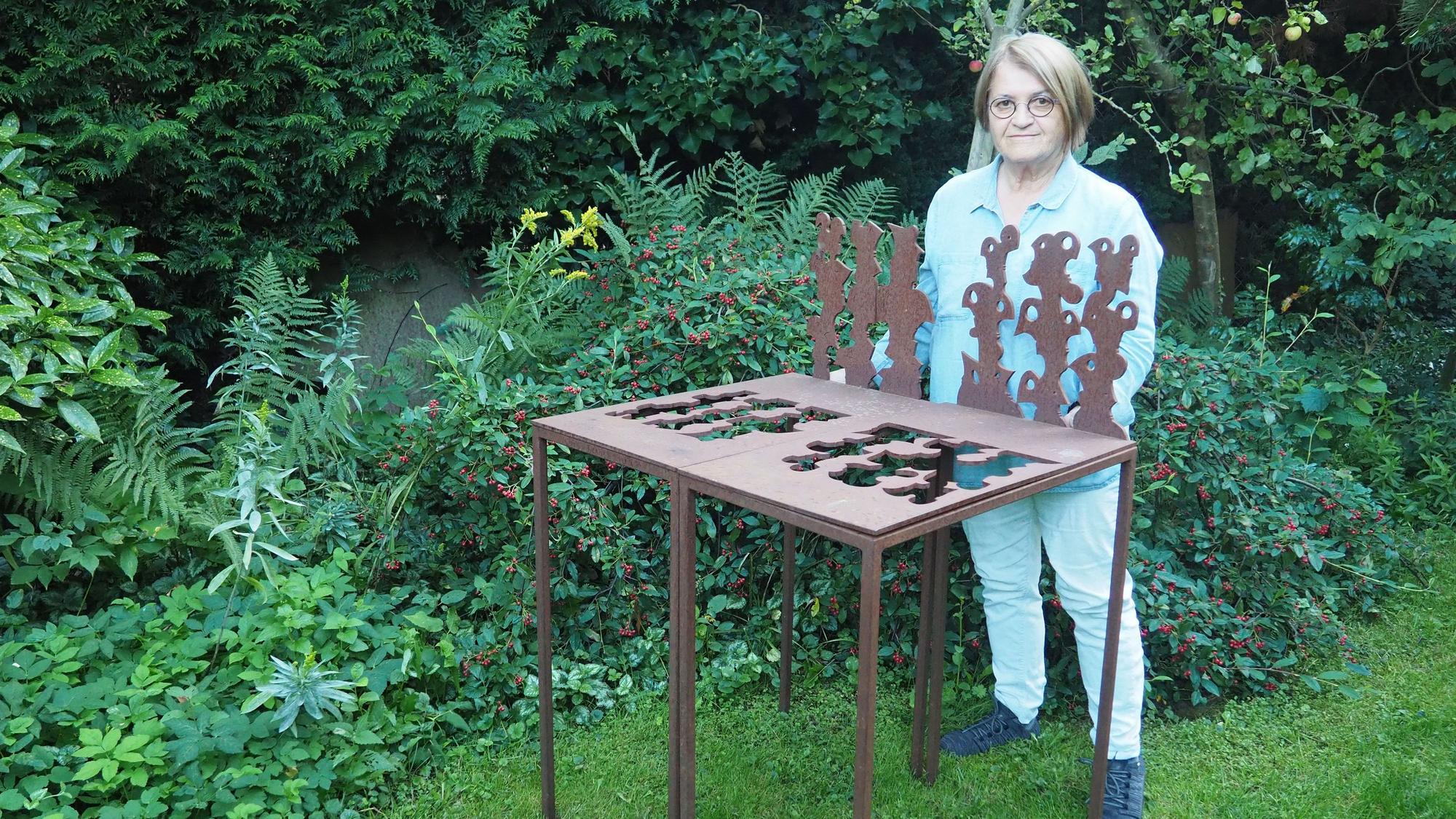 Marti Faber steht im Grünen hinter einer Reihe von Figuren, die sie aus einer Stahlplatte ausgeschnitten hat.
