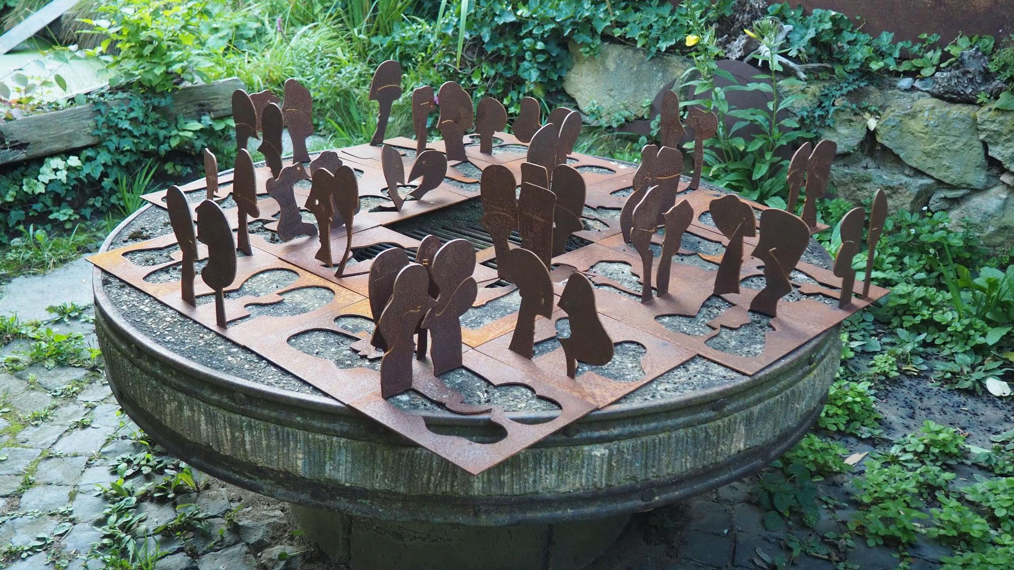 Kleine Stahlquadrate, aus denen Firuren geschnitten sind, sind arrangiert wie auf einen Schachbrett.