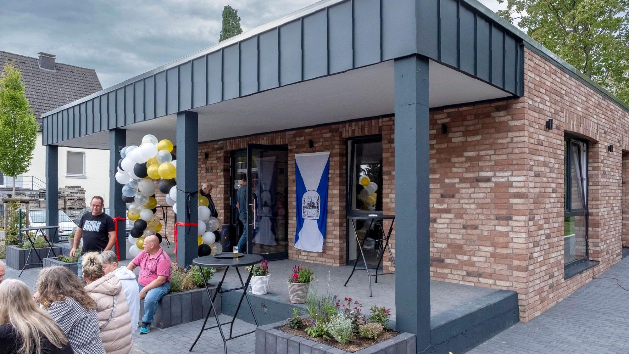 Auf dem Platz vor dem neuen Dorfgemeinschaftshaus in Breitenbenden sitzen einige Personen.