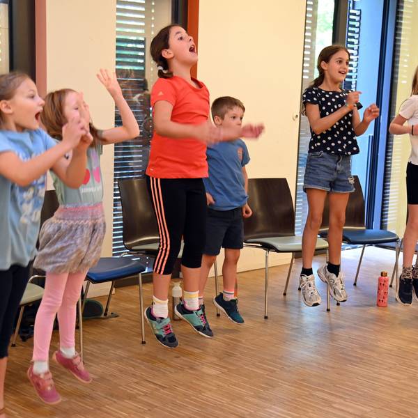 Sechs Kinder srpngen in die Luft, klatschen dabei in die Hände und singen laut.