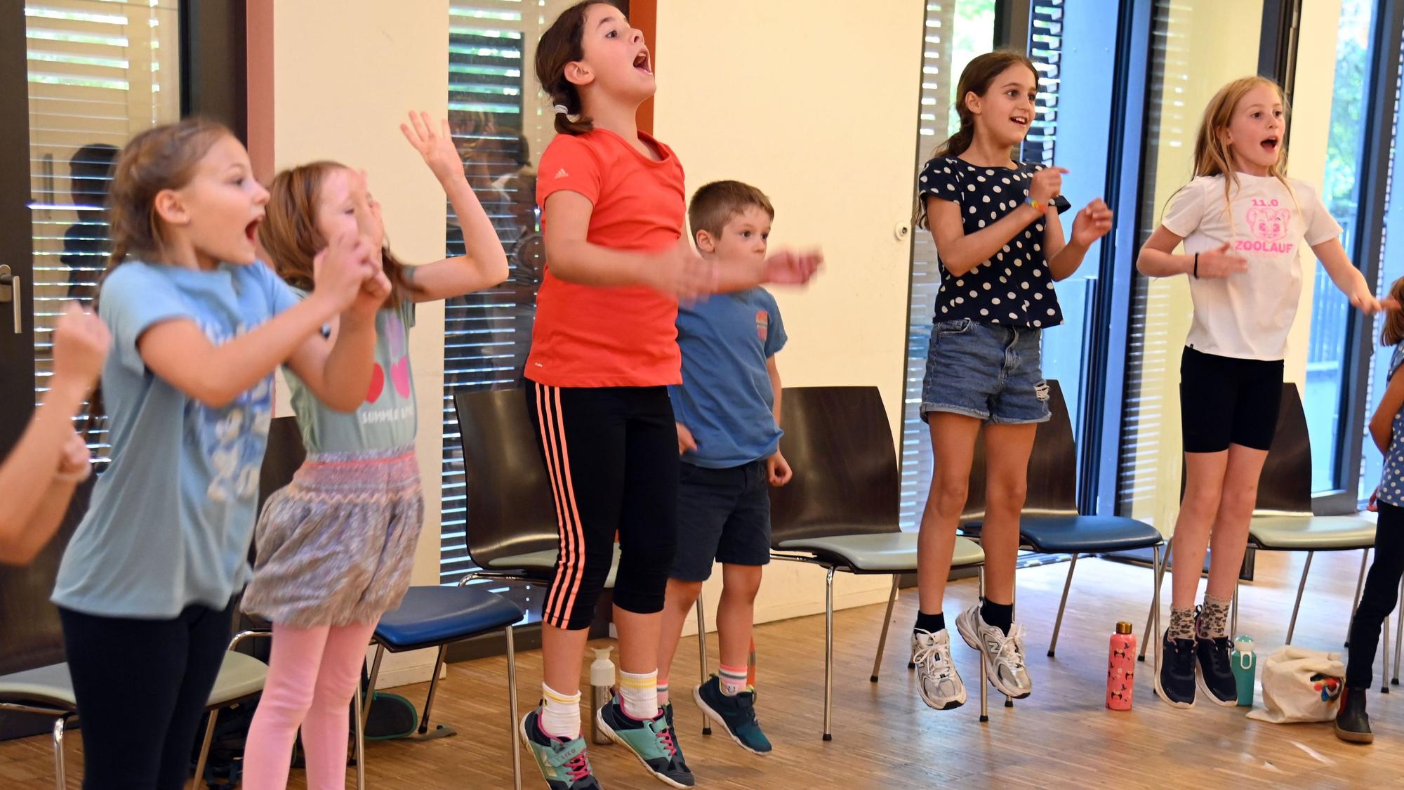 Sechs Kinder srpngen in die Luft, klatschen dabei in die Hände und singen laut.