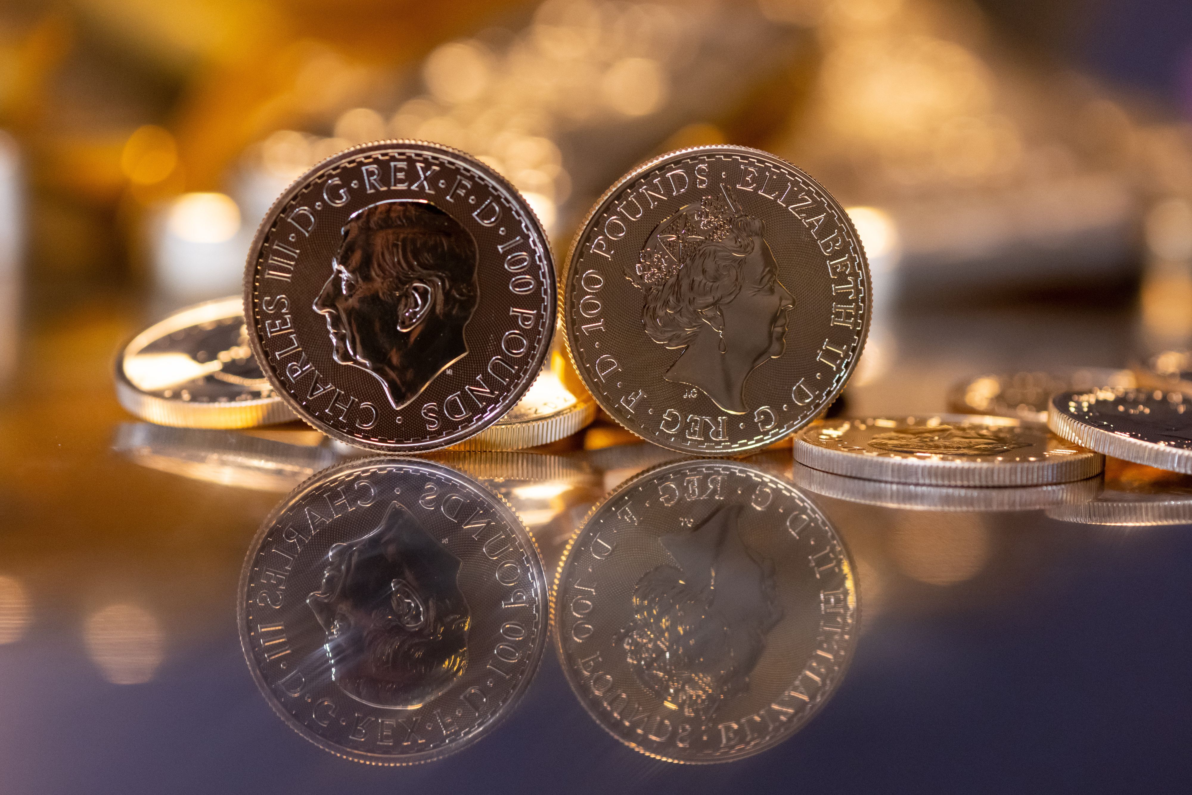Goldbarren und Goldmünzen in unterschiedlicher Größe liegen beim Edelmetallhändler Pro Aurum in einem Tresor auf einem Tisch. Im Vordergrund ist die Goldmünze "Britannia" zu sehen (links mit dem Motiv König Charles III., rechts mit dem Motiv Königin Elizabeth II.)