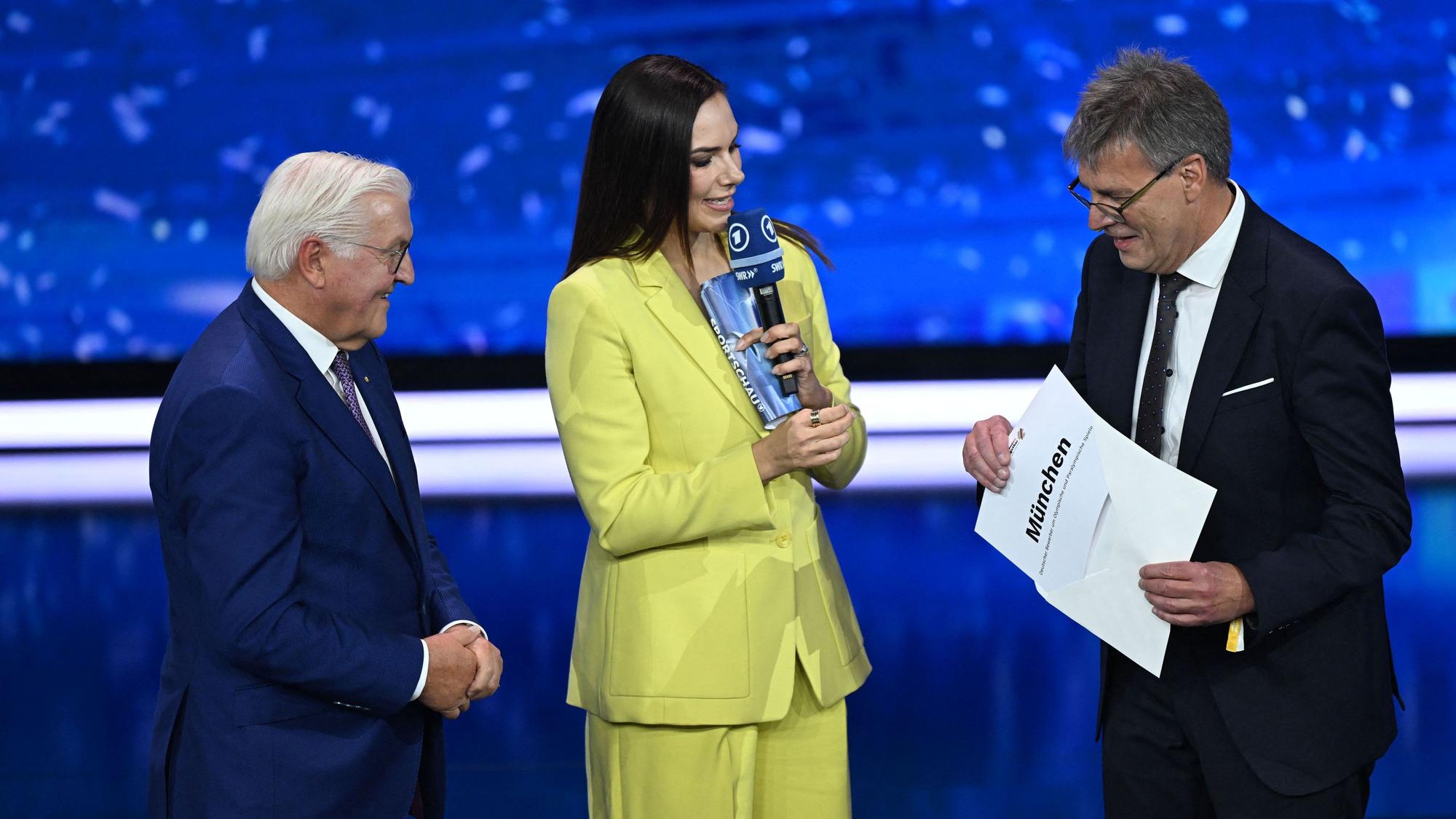 Und er merkt nicht, was er tut: DOSB-Präsident Thomas Weikert nimmt die Ergebnisverkündung vorweg. Bundespräsident Frank-Walter Steinmeier (l.) findet es lustig, Moderatorin Esther Sedlaczek eher nicht.