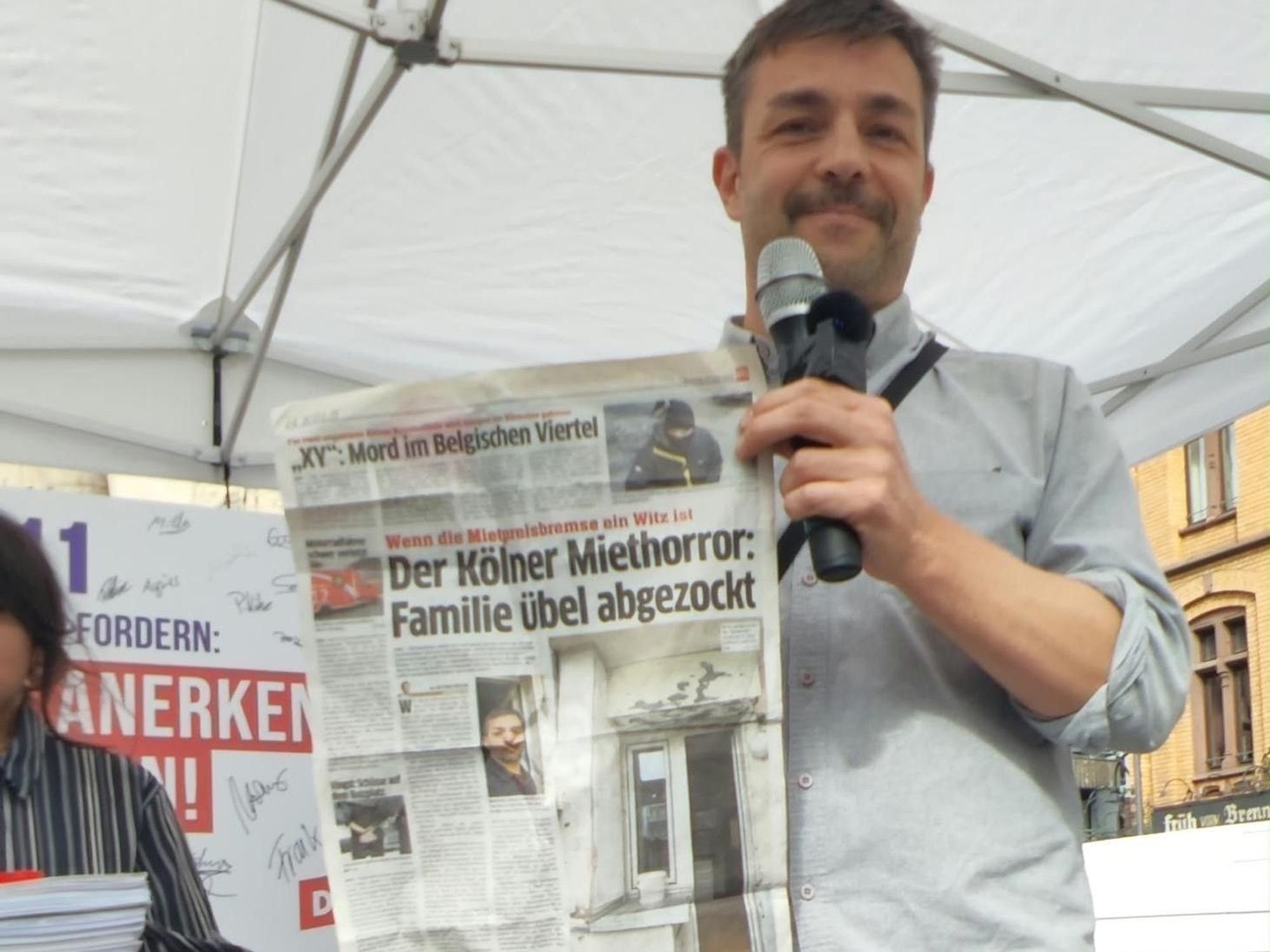 Ein Mann hält einen EXPRESS-Artikel hoch mit der Überschrift „Der Kölner Miethorror: Familie übel abgezockt.“