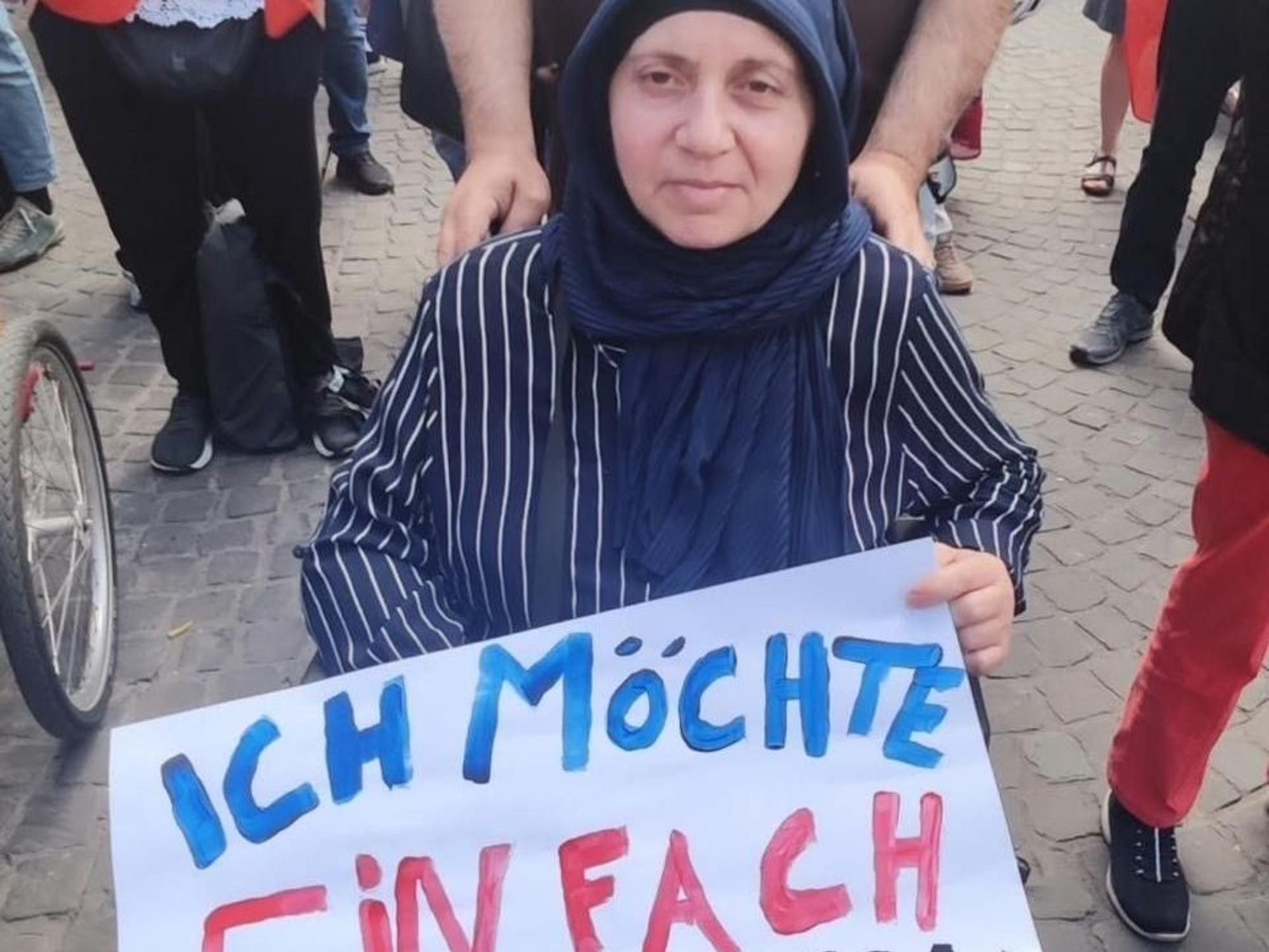 Die Frau, die im Rollstuhl sitzt, hält ein Plakat fest mit der Aufschrift „Ich möchte einfach nur wohnen“.