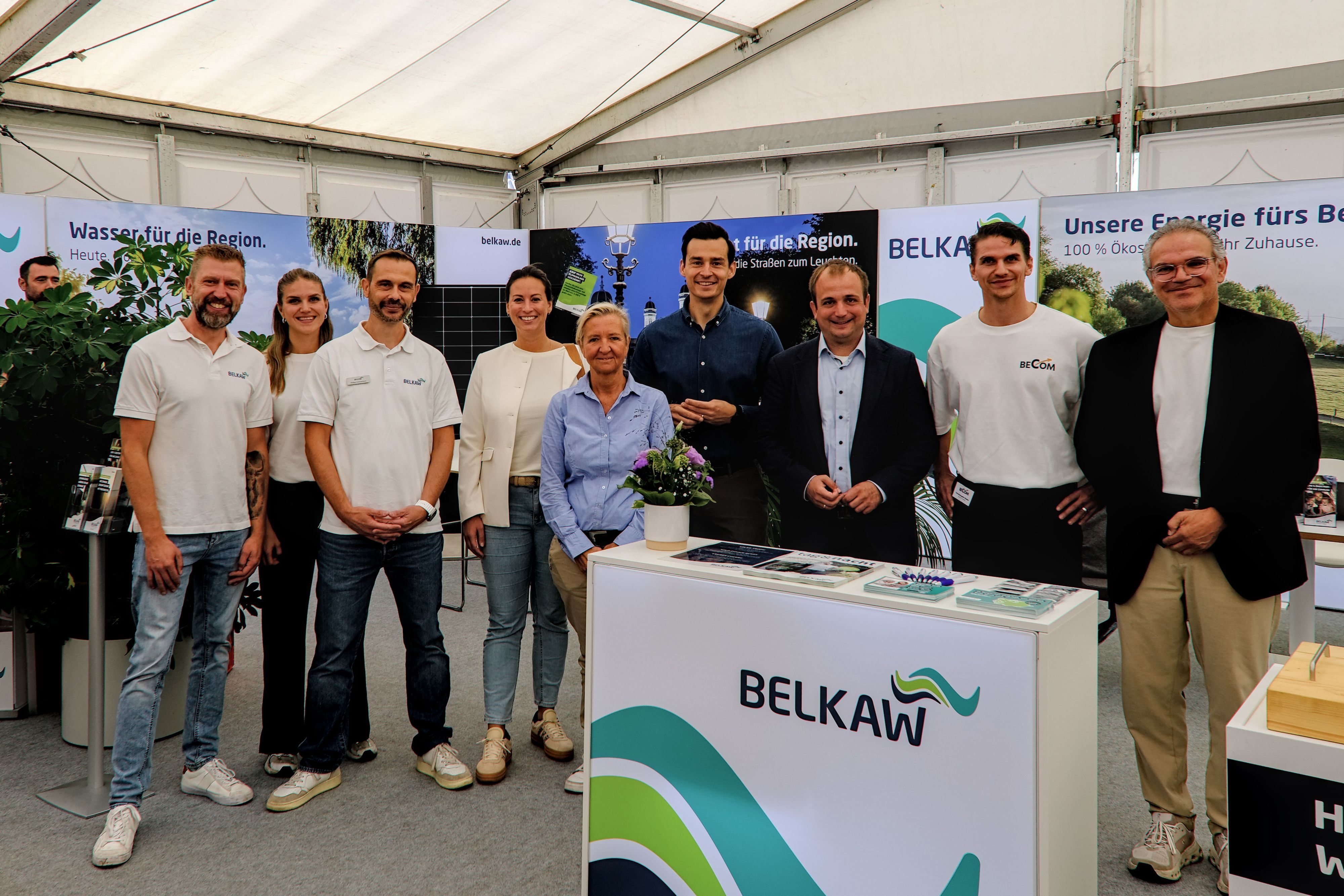 Mehrere Frauen und Männer stehen an einem Stand mit der Aufschrift Belkaw