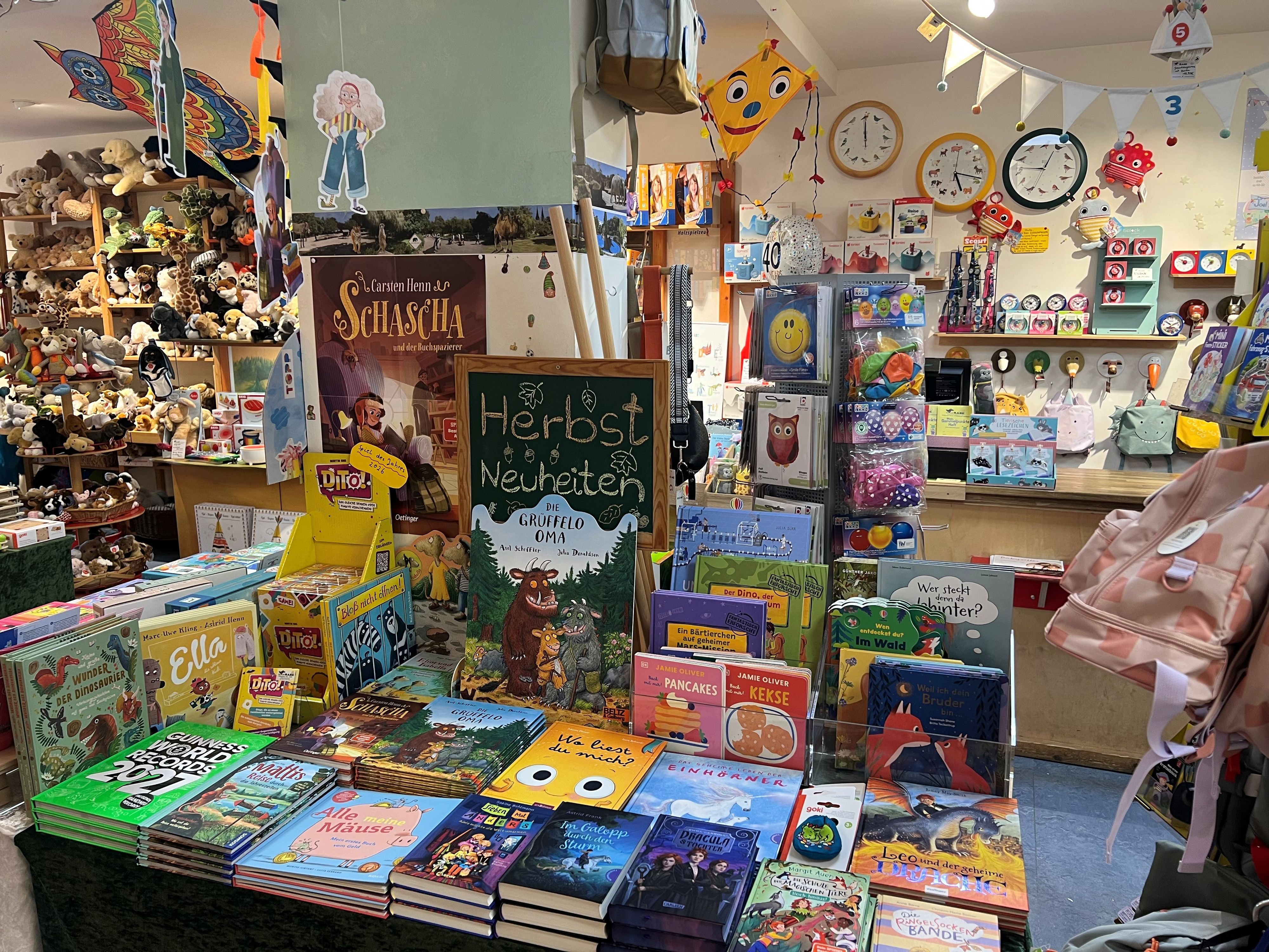 Blick in eine Buchhandlung mit Tischen voller Kinderbücher, Spielzeug und Plüschtieren. Vorn ist unter anderem „Die Grüffelo-Oma“ ausgestellt.