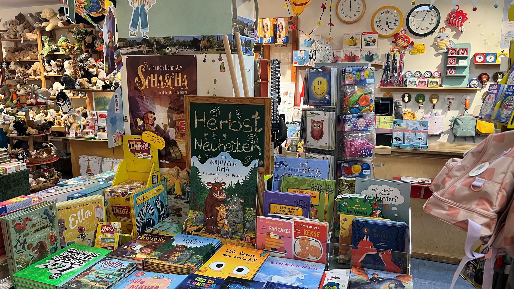 Blick in eine Buchhandlung mit Tischen voller Kinderbücher, Spielzeug und Plüschtieren. Vorn ist unter anderem „Die Grüffelo-Oma“ ausgestellt.